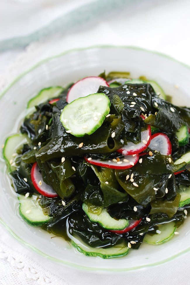 Seaweed 桌布 壁紙 — 一碗光澤的海藻沙律，上面放有青瓜、蘿蔔和芝麻，放在蕾絲枱布上。