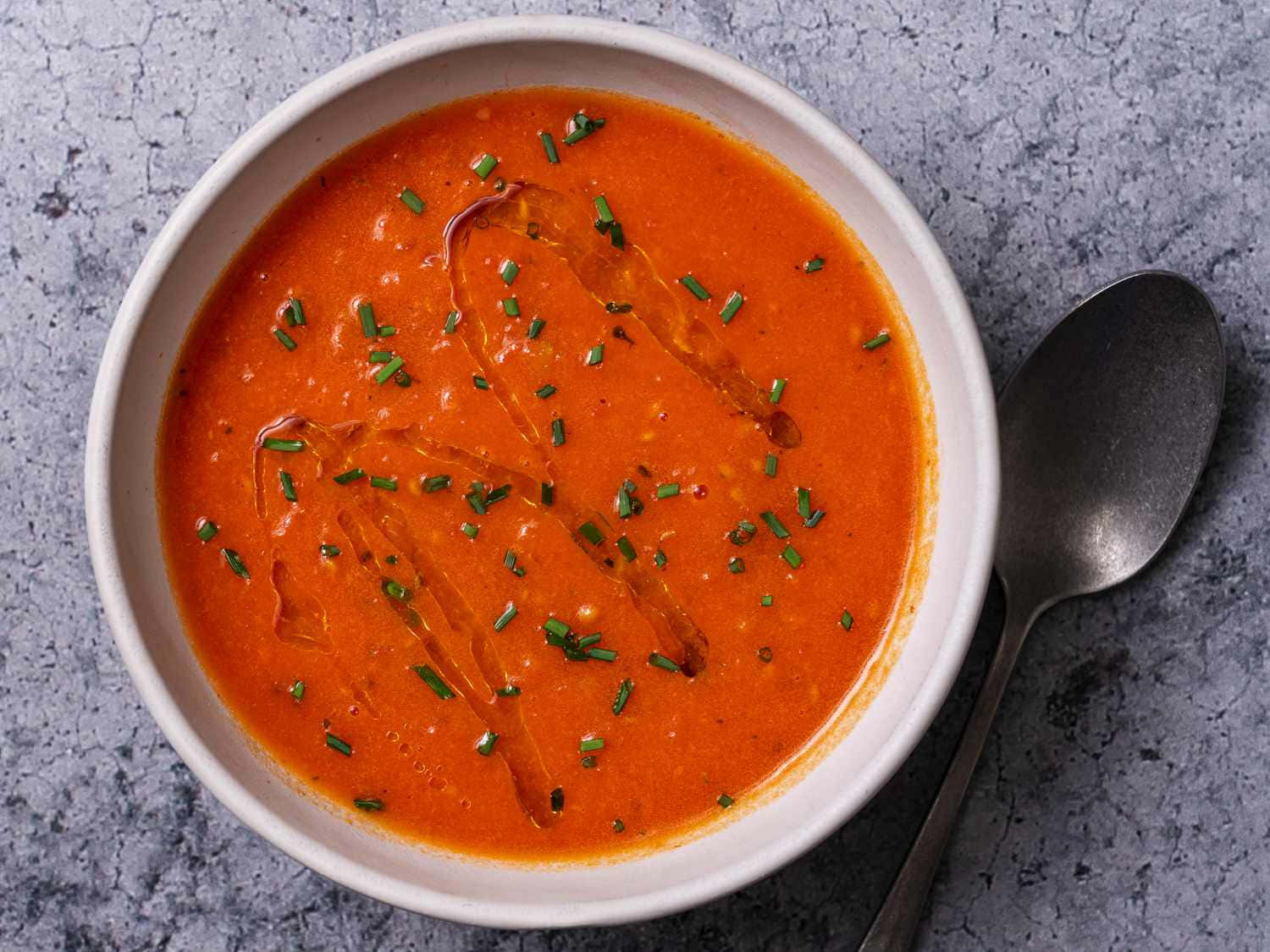 Soup 桌布 壁紙 — 一碗奶油橙色湯，飾以切碎的細香蔥和淋上橄欖油，放在白色碗中，置於灰色石面上，旁邊放著湯匙。