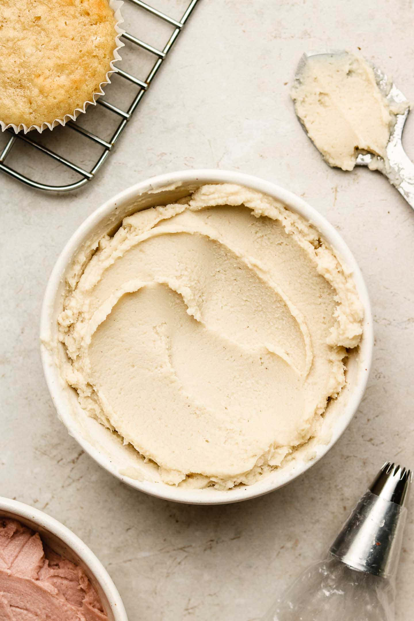 Buttercream 桌布 壁紙 — 一碗奶油米色糖霜放在淺色枱面上，旁邊有一個正在冷卻的杯子蛋糕和擠花工具。