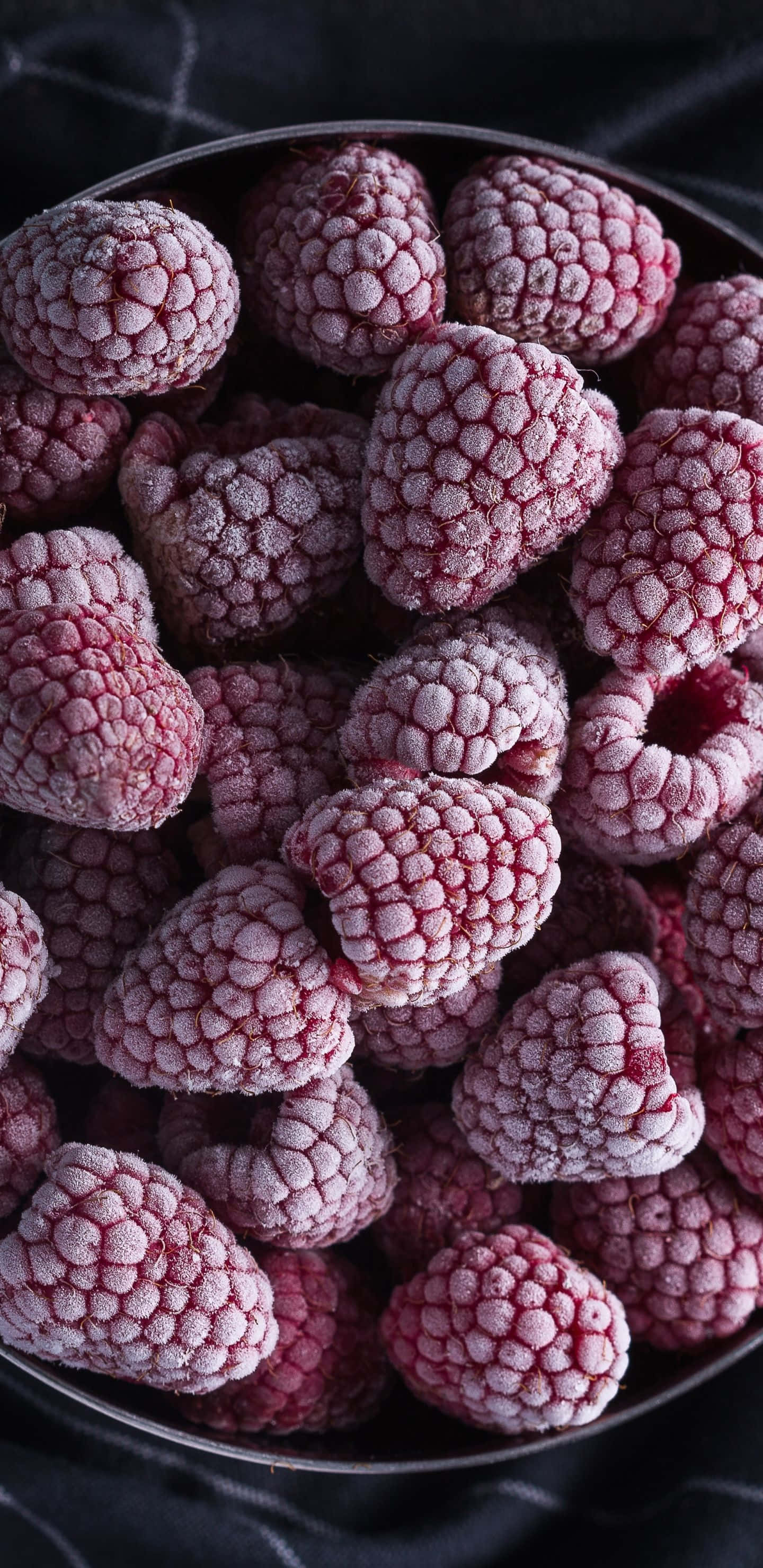 一碗新鮮採摘的紅覆盆子 壁紙 — 特寫鏡頭：結霜的覆盆子堆放在金屬碗中，背景為深色紋理。