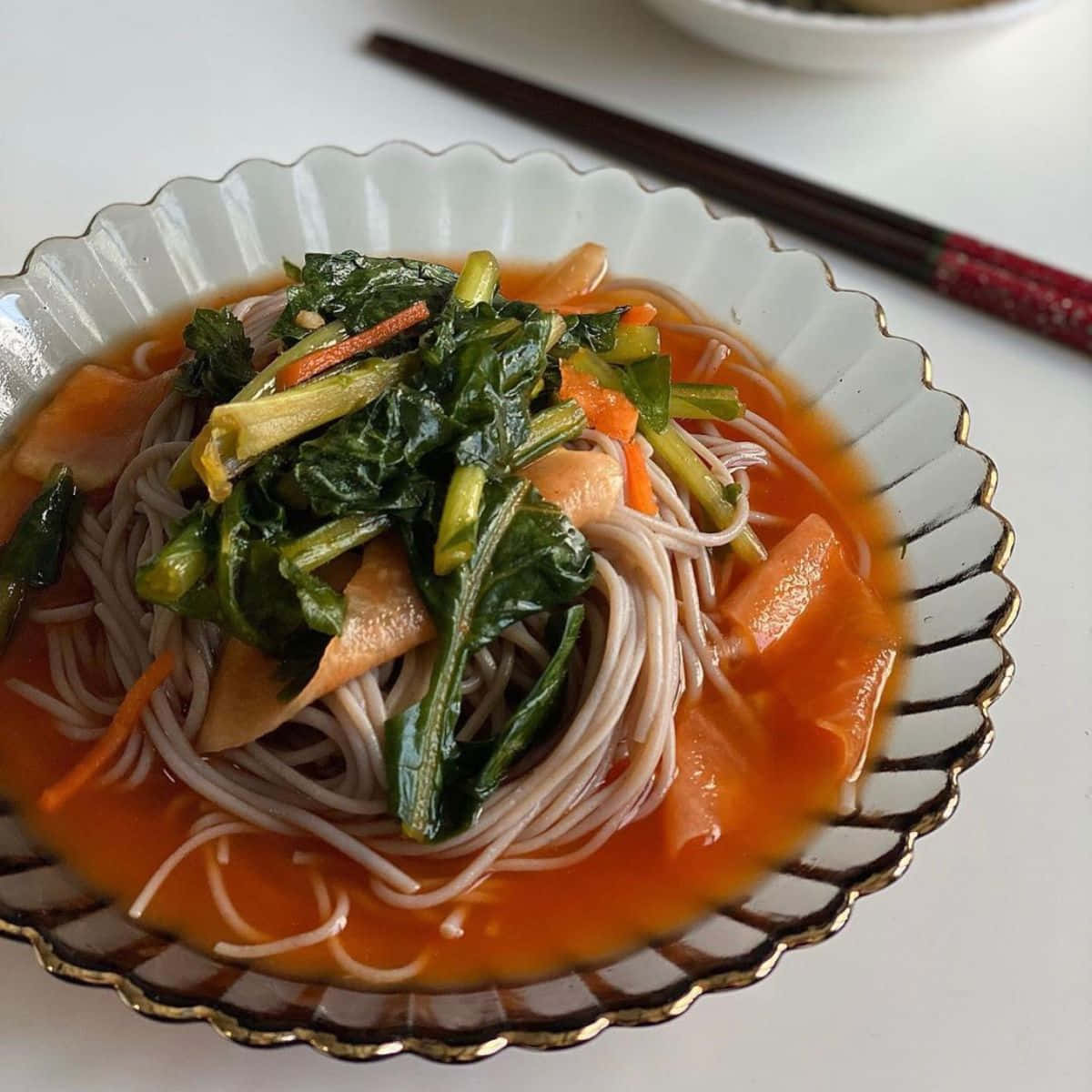 Minimalist Food 桌布 壁紙 — 一碗橙色湯底蕎麥麵的特寫，上面放有菠菜和胡蘿蔔片。