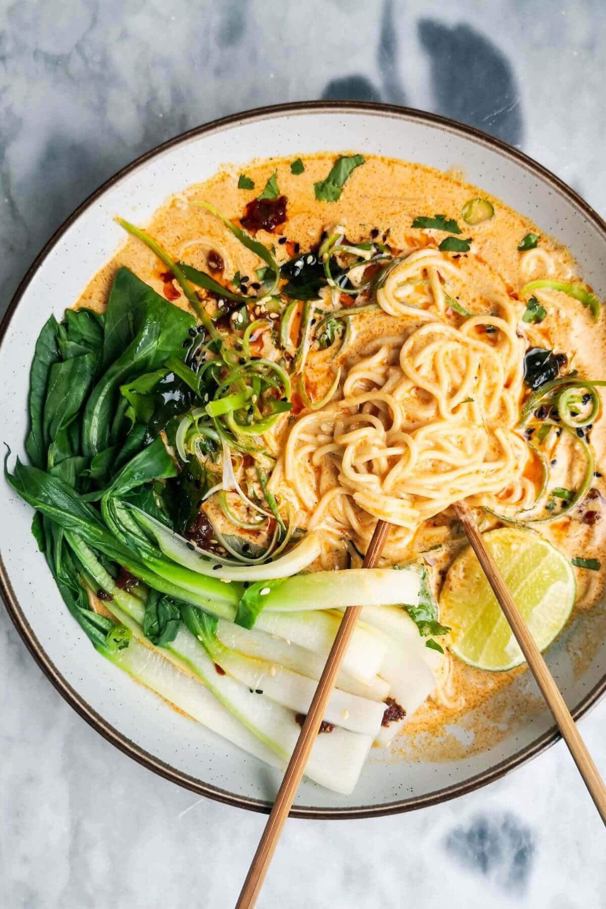 Noodles 桌布 壁紙 — 一碗熱騰騰的奶油咖喱湯麵，配上新鮮蔬菜、青檸和辣椒油，筷子準備好享用。