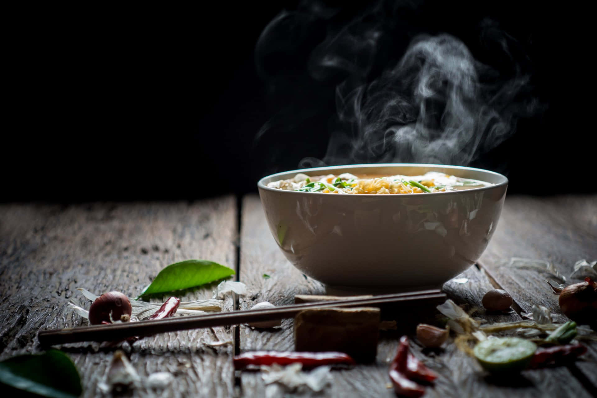 Winter Food 桌布 壁紙 — 一碗熱騰騰的湯麵放在質樸的木桌上，周圍是新鮮的香草和香料。