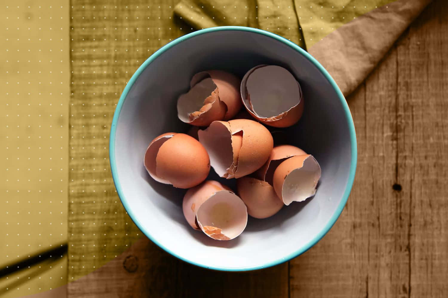 Egg 桌布 壁紙 — 一碗碎咗嘅啡色雞蛋殼放喺木枱上面，旁邊有塊黃色布。
