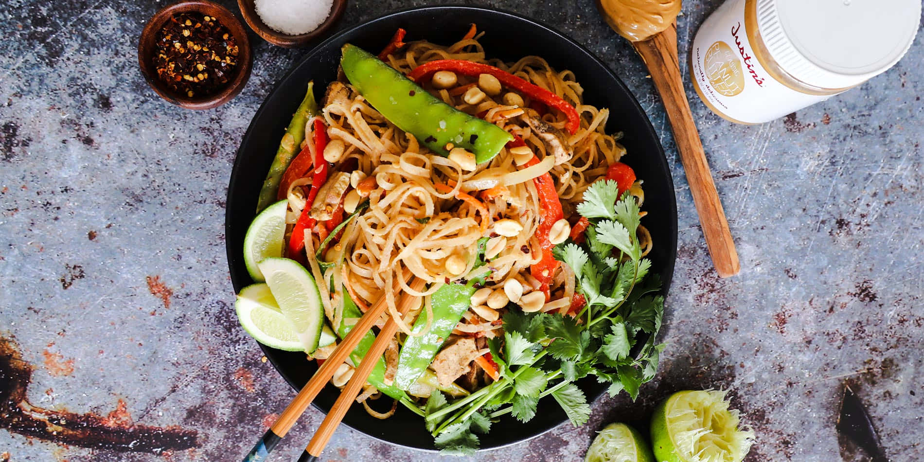 Noodles 桌布 壁紙 — 一碗色彩繽紛的炒麵，配上花生、辣椒、青檸和新鮮香草，放在質樸的金屬表面上。