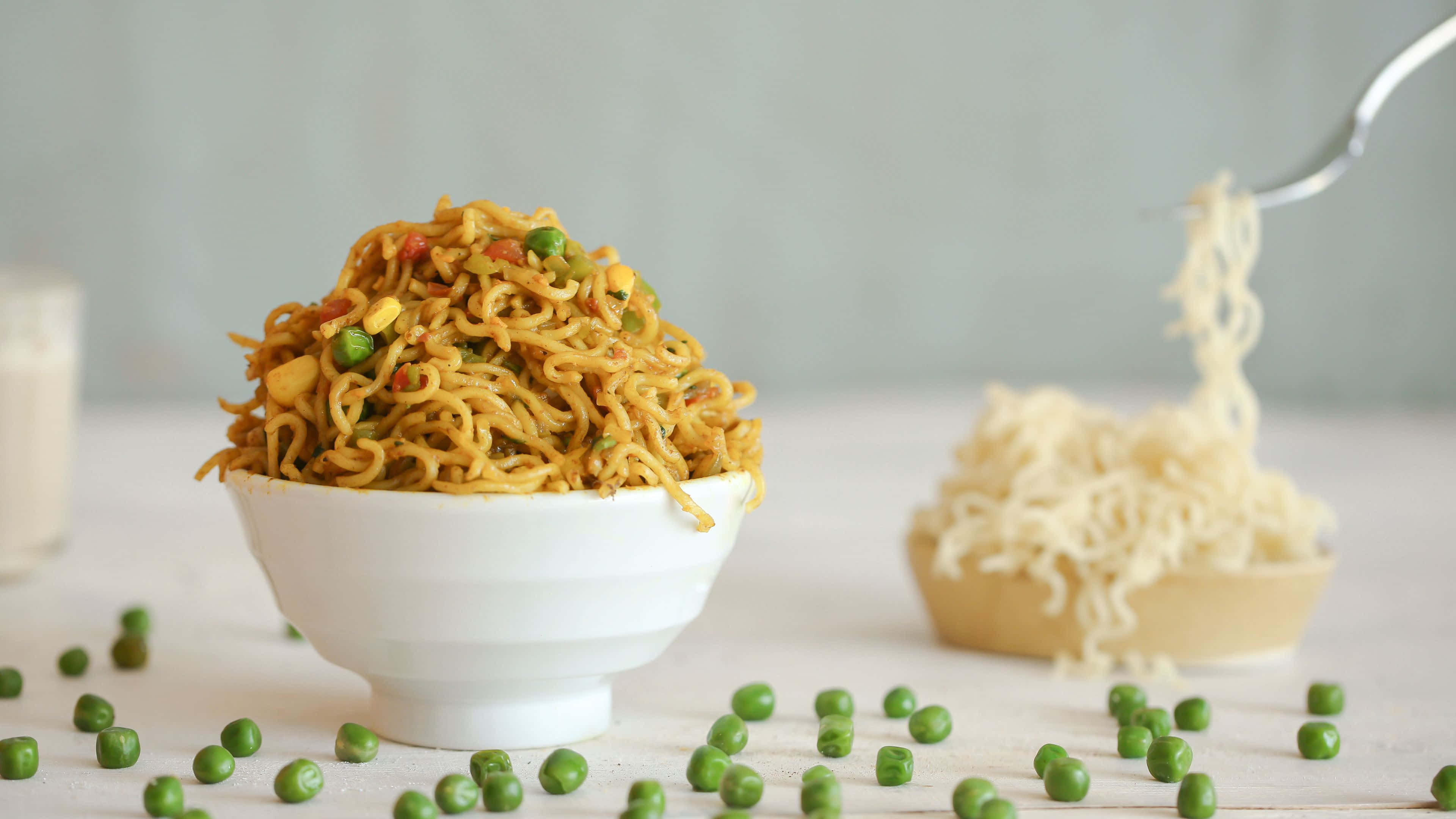 Noodles 桌布 壁紙 — 一碗色彩繽紛的蔬菜麵，配上青豆，旁邊有一碗普通麵條，叉子正挑起麵條。