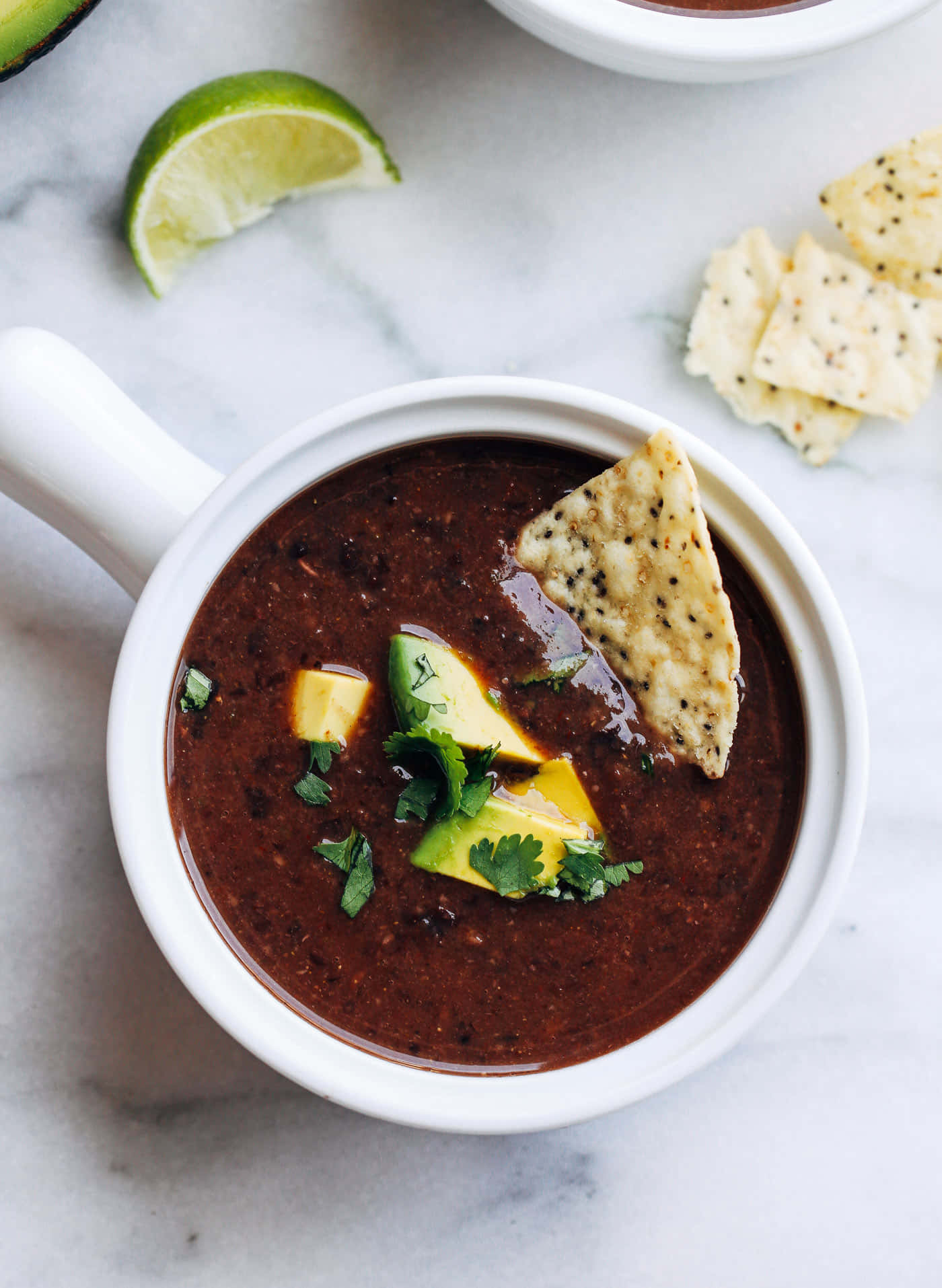Black Bean Soup 桌布 壁紙 — 一碗豐富的黑豆湯，上面放有牛油果、青檸和芫荽，放在大理石表面上，旁邊有玉米片。