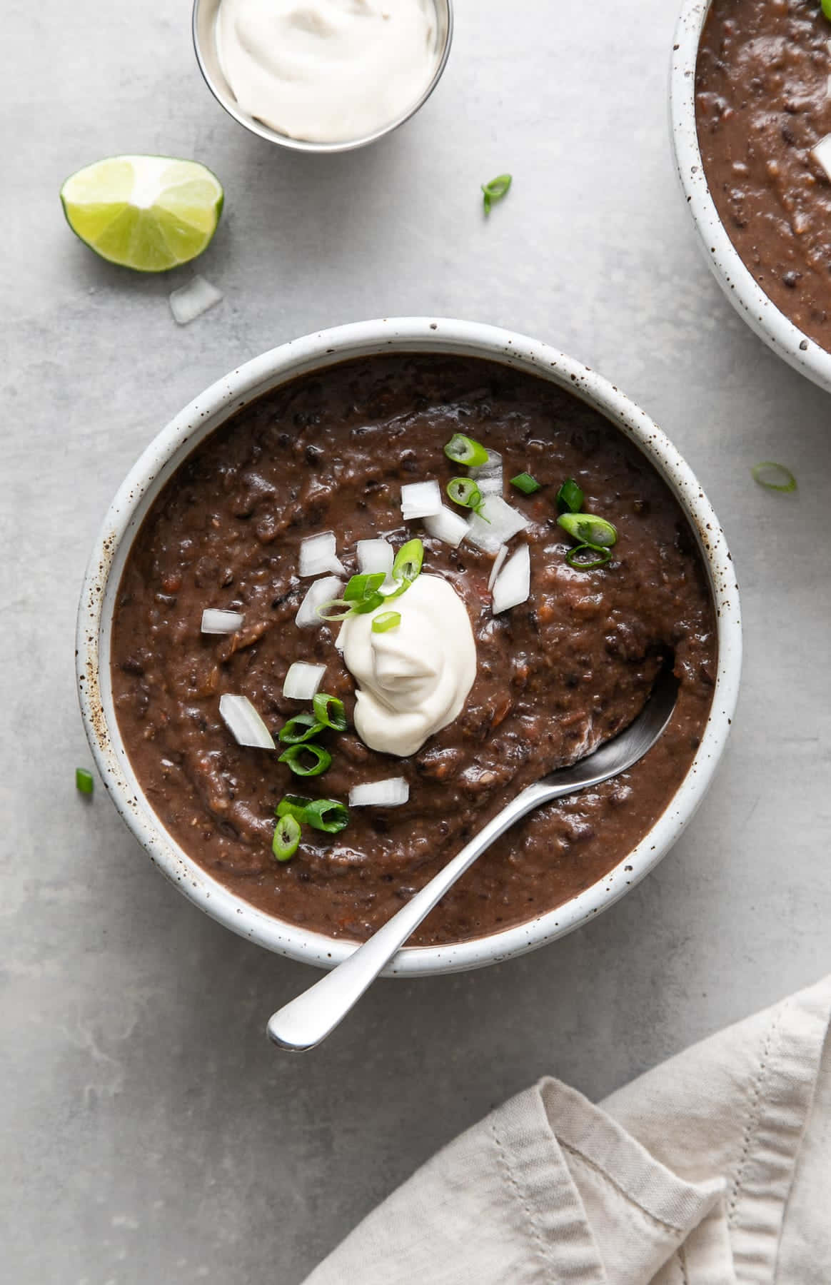 Black Bean Soup 桌布 壁紙 — 一碗鄉村風味濃郁黑豆湯，上面放有酸奶油、切碎青蔥和青檸角，置於淺灰色表面上。