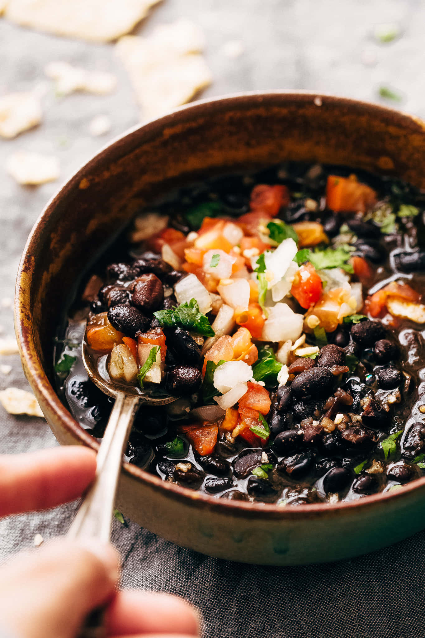 Black Bean Soup 桌布 壁紙 — 一碗鄉村風味的黑豆湯，上面放有新鮮切粒番茄、洋蔥和芫荽，正用湯匙攪拌。