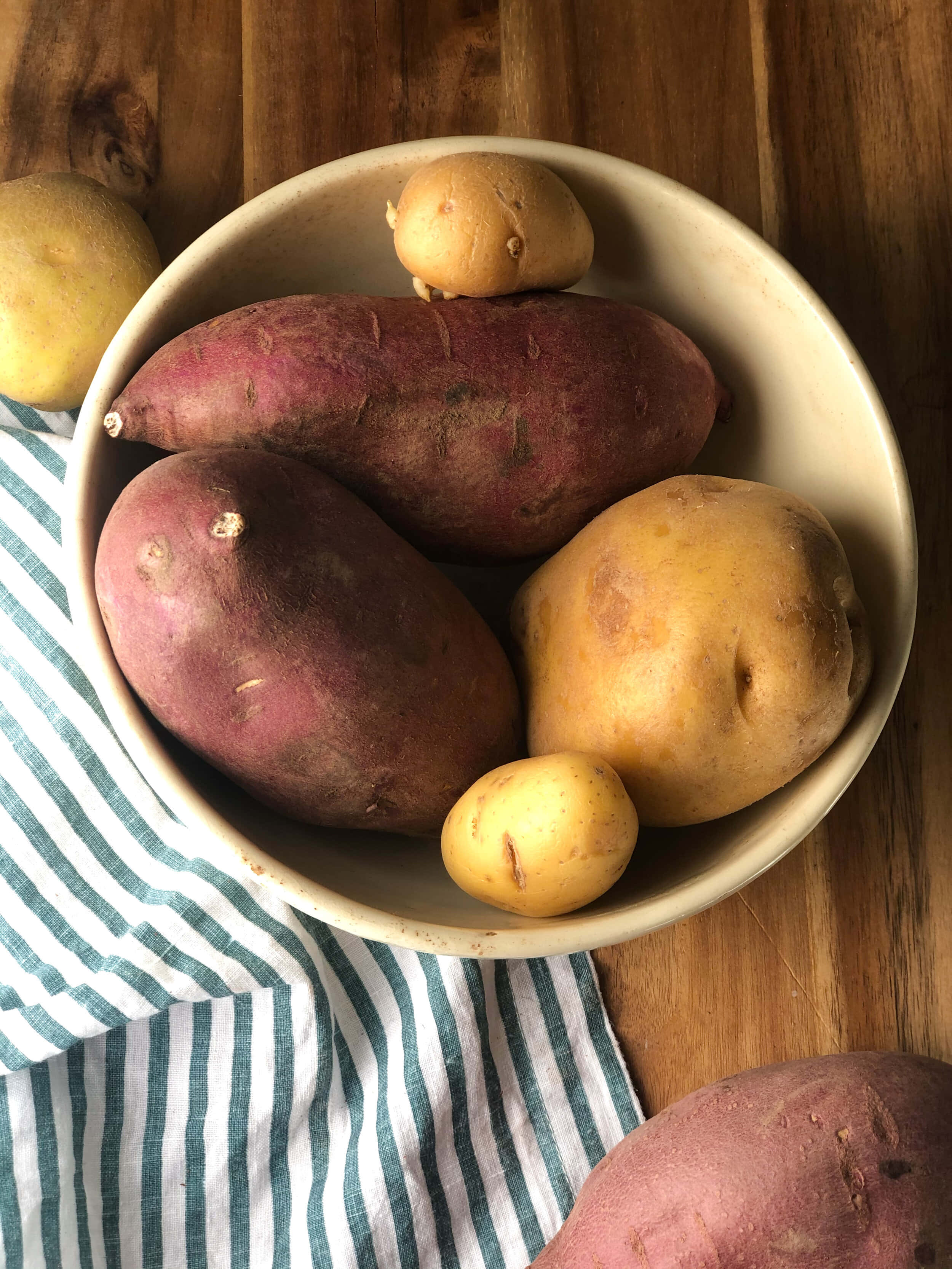 Red Potatoes 桌布 壁紙 — 一碗雜錦薯仔和番薯放在木桌上的一塊條紋布上。