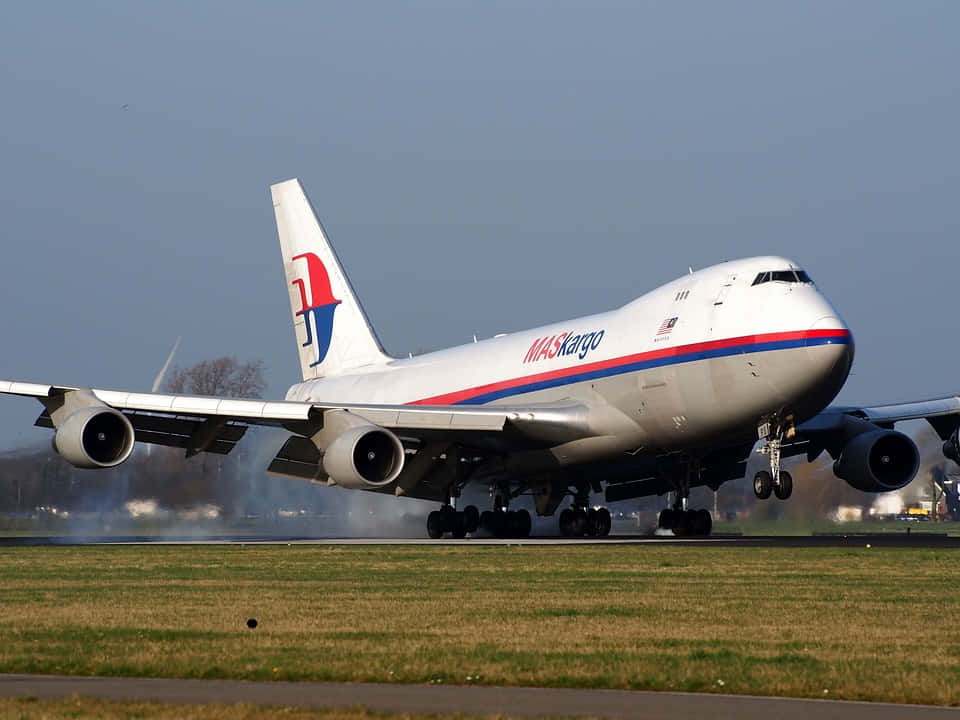 MASkargo波音747貨機在跑道上降落，草地和陰天。