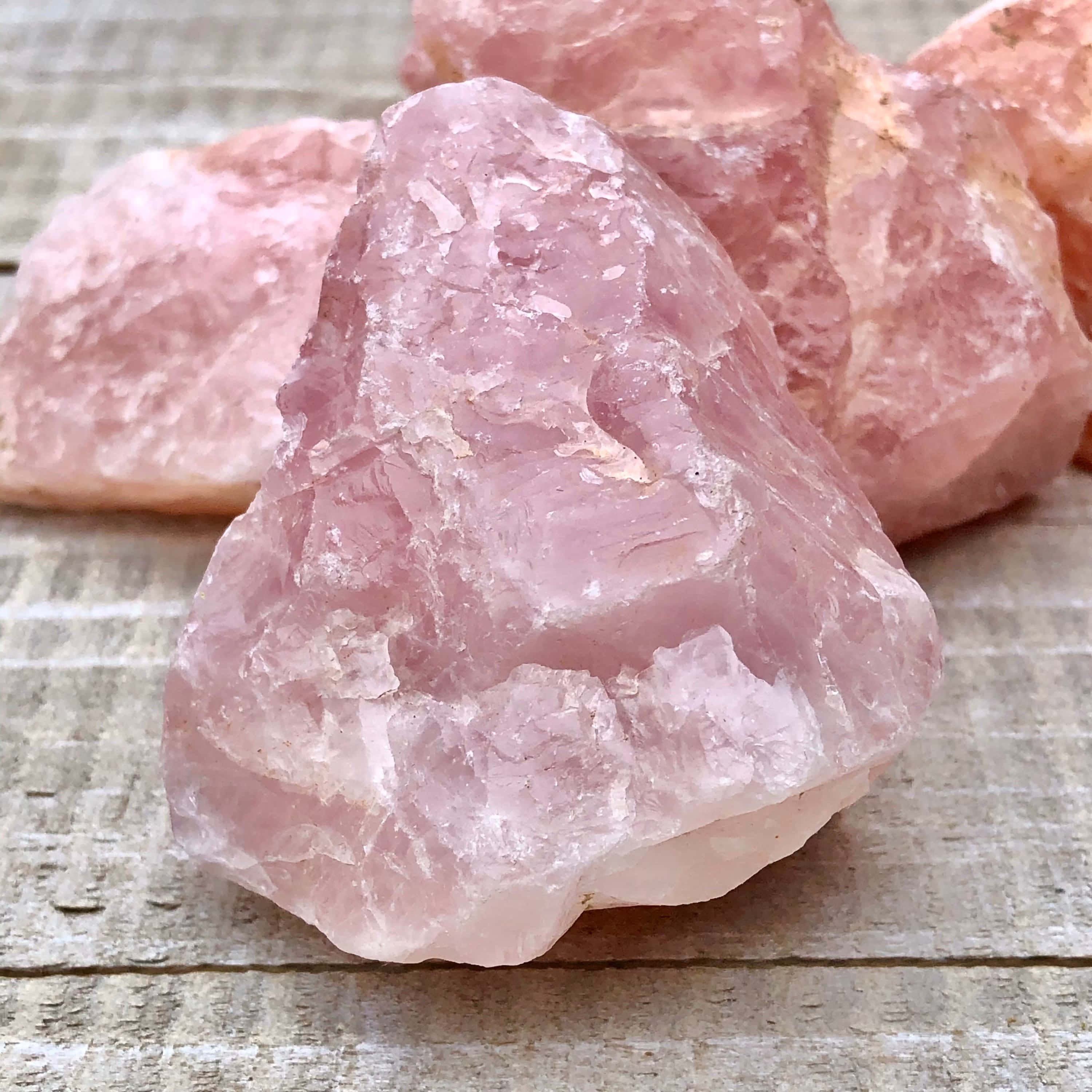 Pink Crystal Quartz 桌布 壁紙 — 一簇未經打磨的粉紅玫瑰石英晶體，在柔和自然光下，靜置於風化木質表面上。