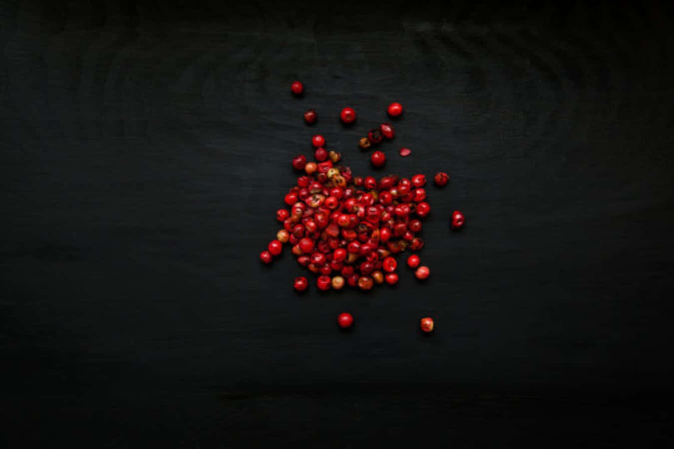 Pink Peppercorn 桌布 壁紙 — 一簇鮮紅的胡椒粒散落在深色紋理表面上。