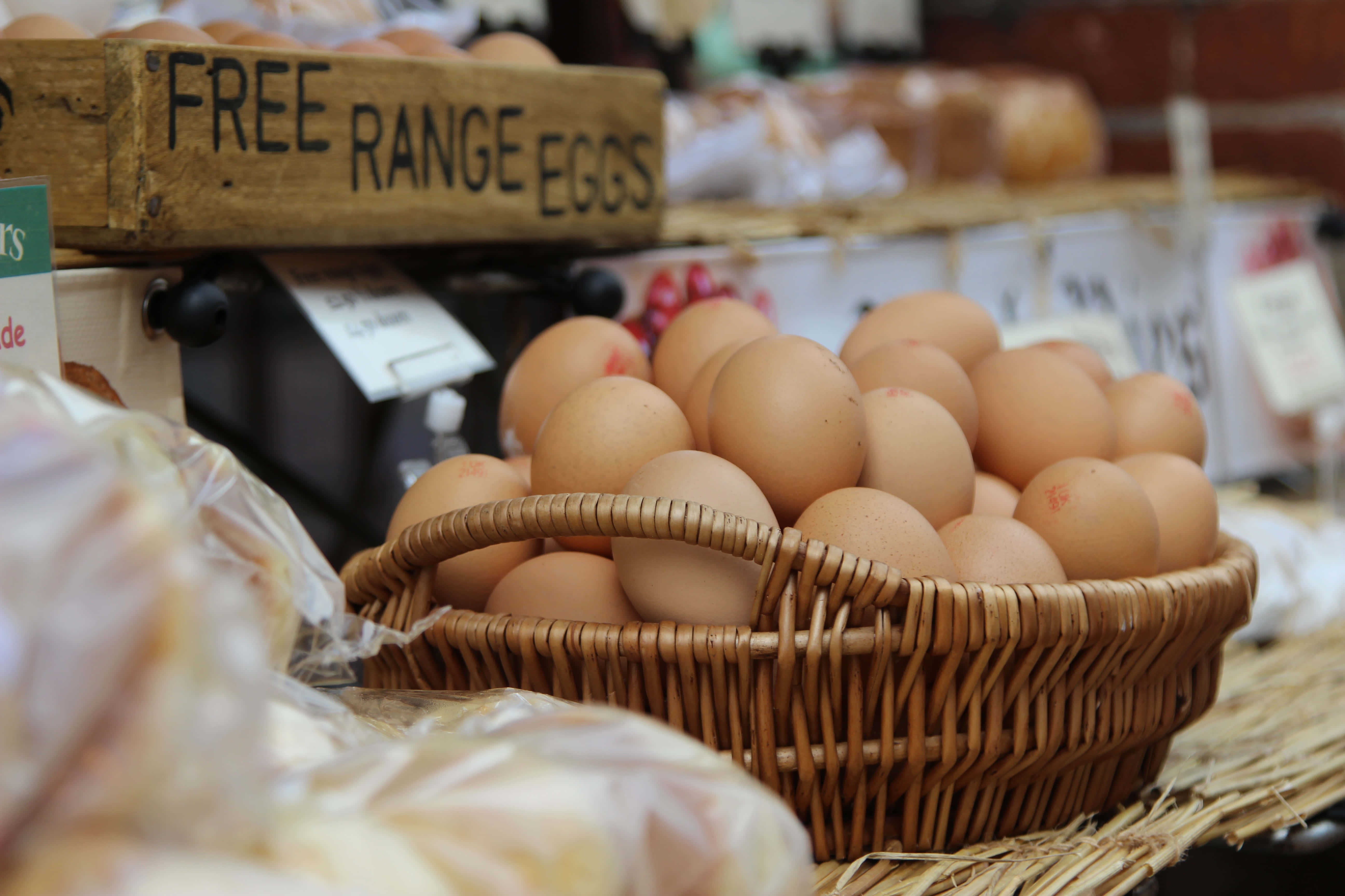 Brown Eggs 桌布 壁紙 — 一籃啡色自由放養雞蛋放在一個市場攤位上，上方有一個木牌。