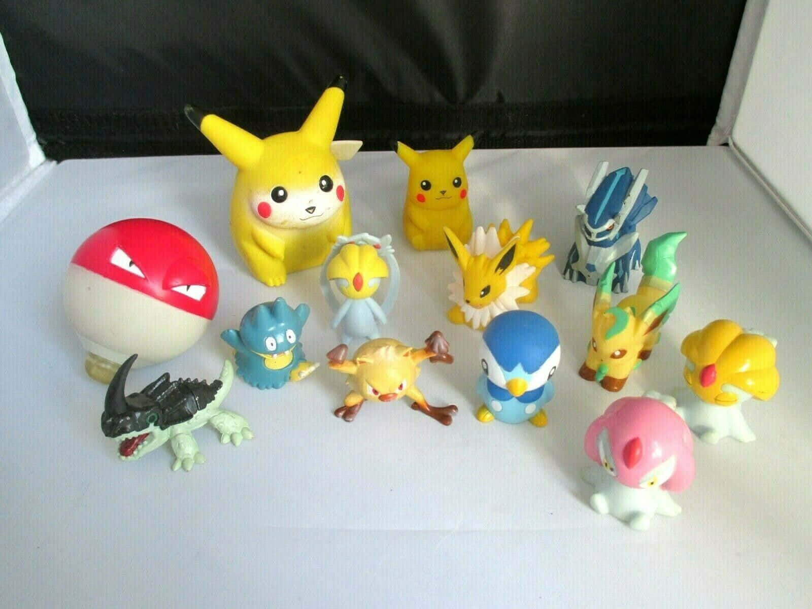 Pokemon Figures 桌布 壁紙 — 一系列色彩繽紛的寵物小精靈公仔和一個精靈球排列在白色表面上，背景為黑色。