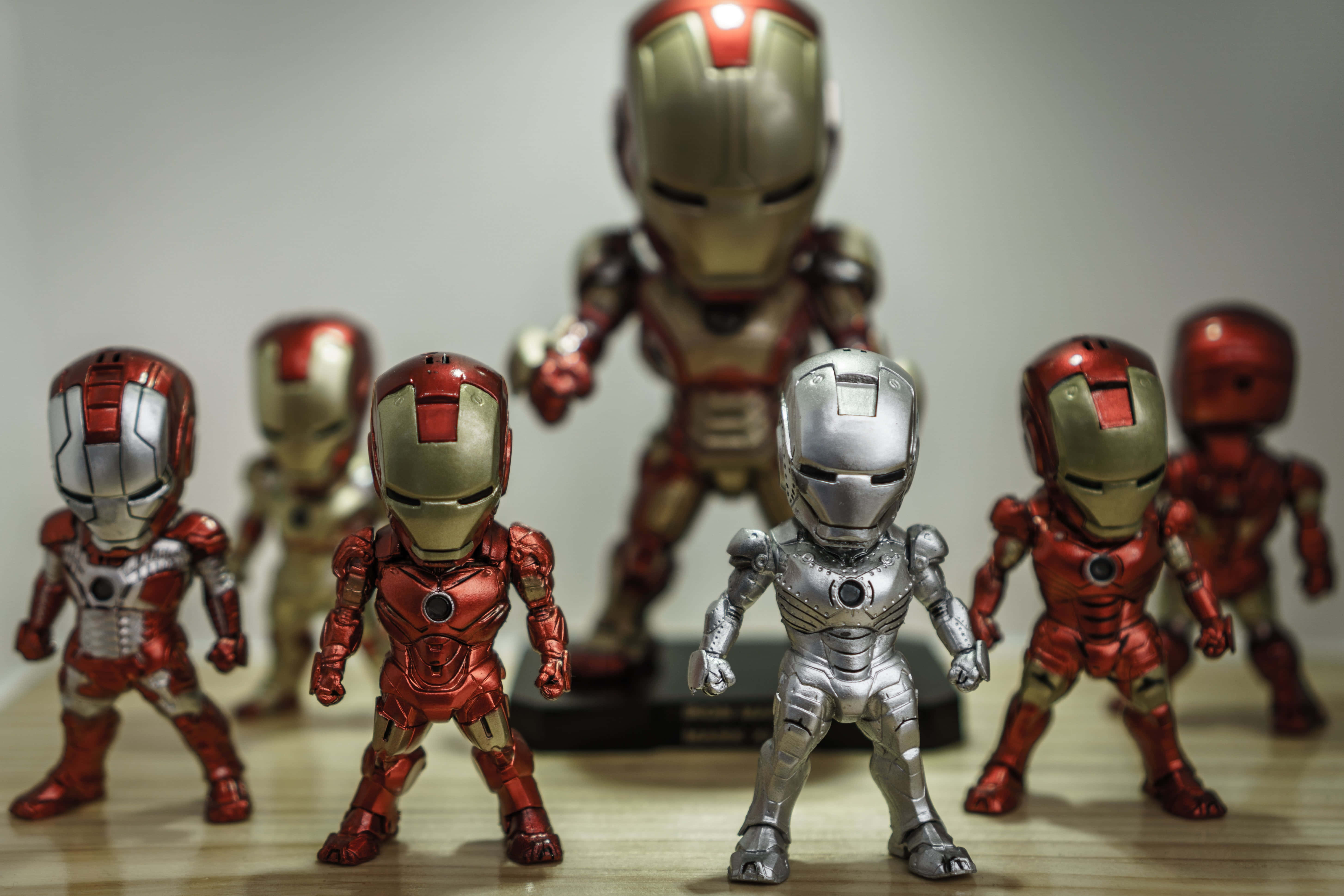 Iron Man Action Figures 桌布 壁紙 — 一系列身穿紅色、金色和銀色盔甲的鐵甲奇俠動作人偶，在柔和的工作室燈光下擺放在木質表面上。