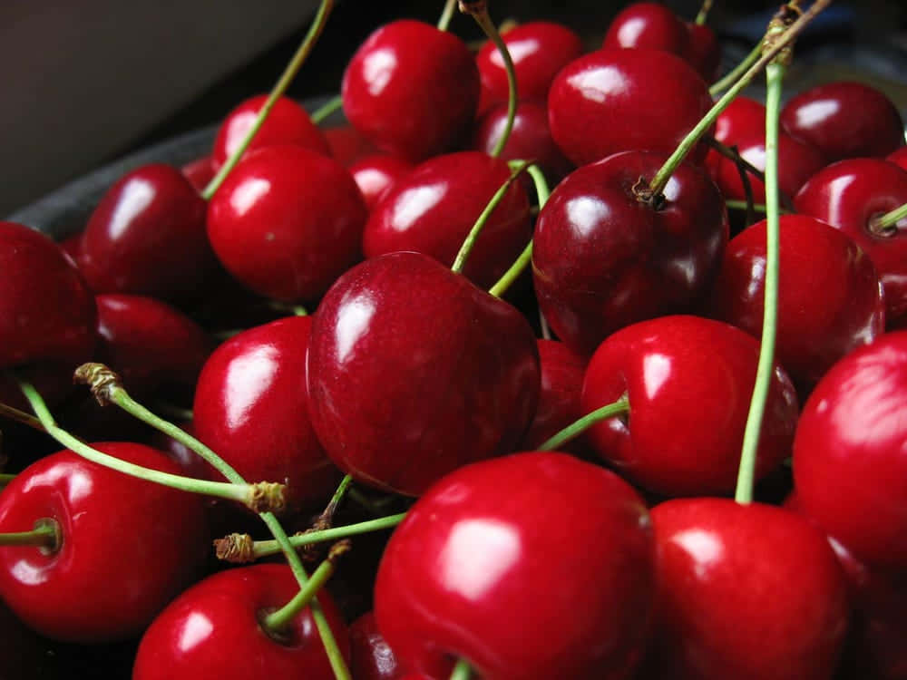 Red Fruit 桌布 壁紙 — 一組帶有綠色莖的亮紅色櫻桃的特寫，堆疊在一起，光滑的表面捕捉到明亮的光線。