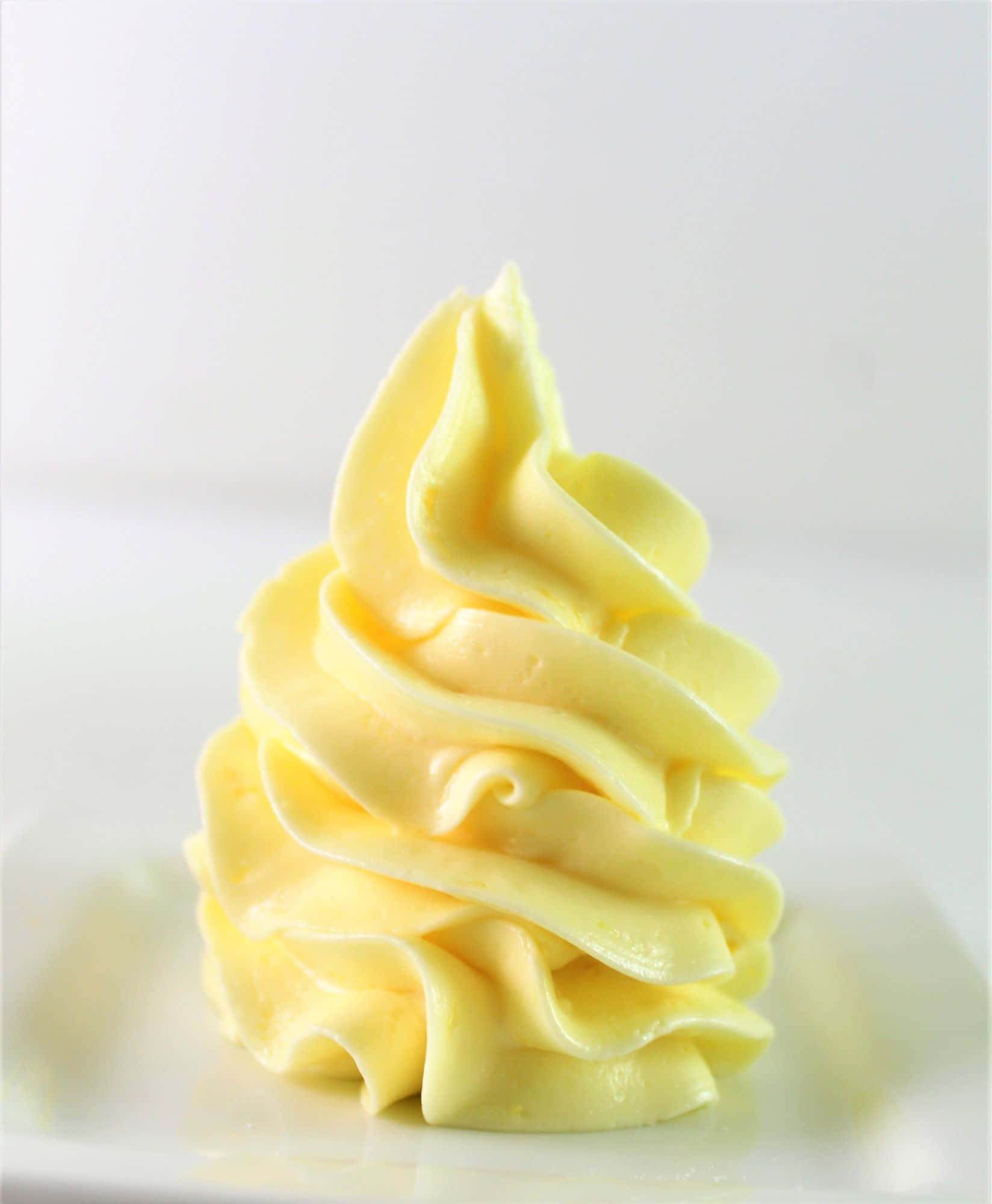 Buttercream 桌布 壁紙 — 一縷完美的淡黃色忌廉優雅地放在白色碟子上，背景柔和模糊。