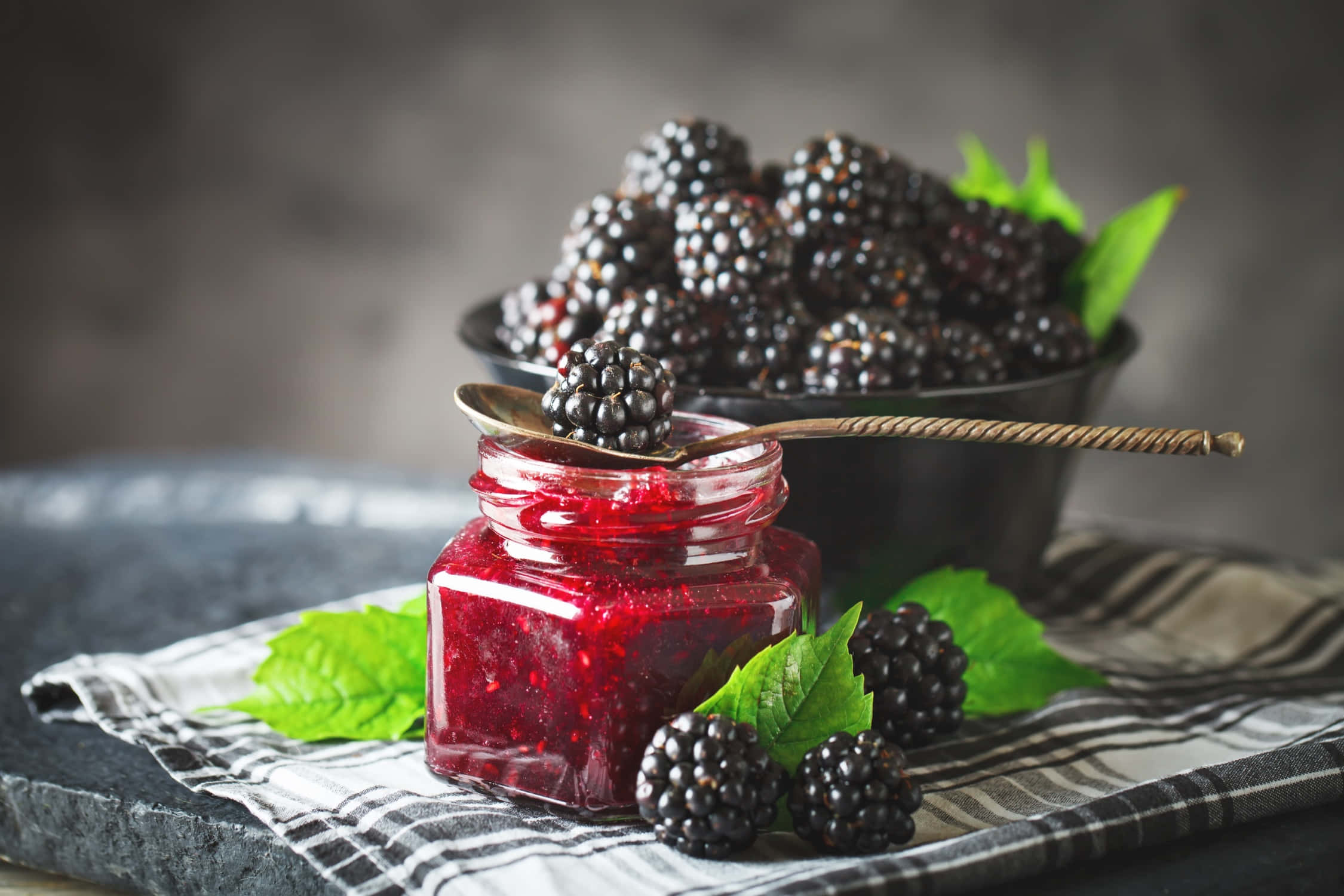 Blackberry Jam 桌布 壁紙 — 一罐有光澤的黑莓果醬放在條紋布上，旁邊是新鮮莓果和薄荷葉。