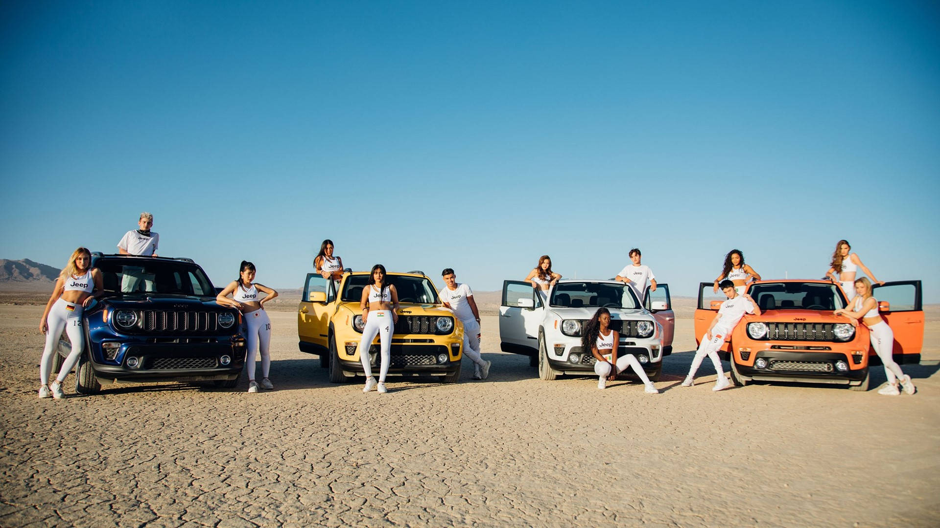 Now United x Jeep Renegade 壁紙 — 一群人在晴朗藍天下，自信地站在廣闊沙漠中色彩繽紛的吉普車旁擺姿勢。