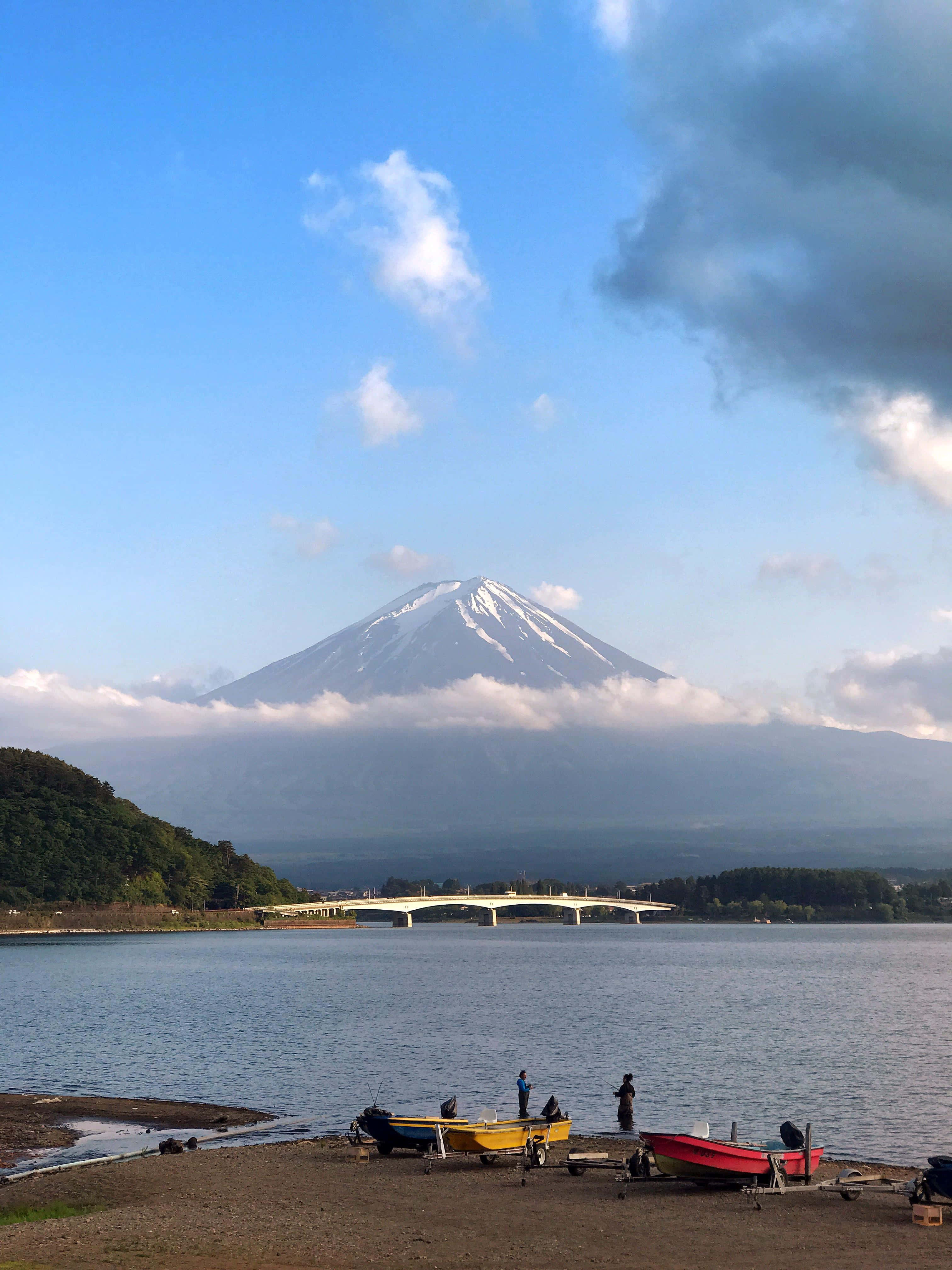 一群人坐喺岸邊，後面有座山 壁紙