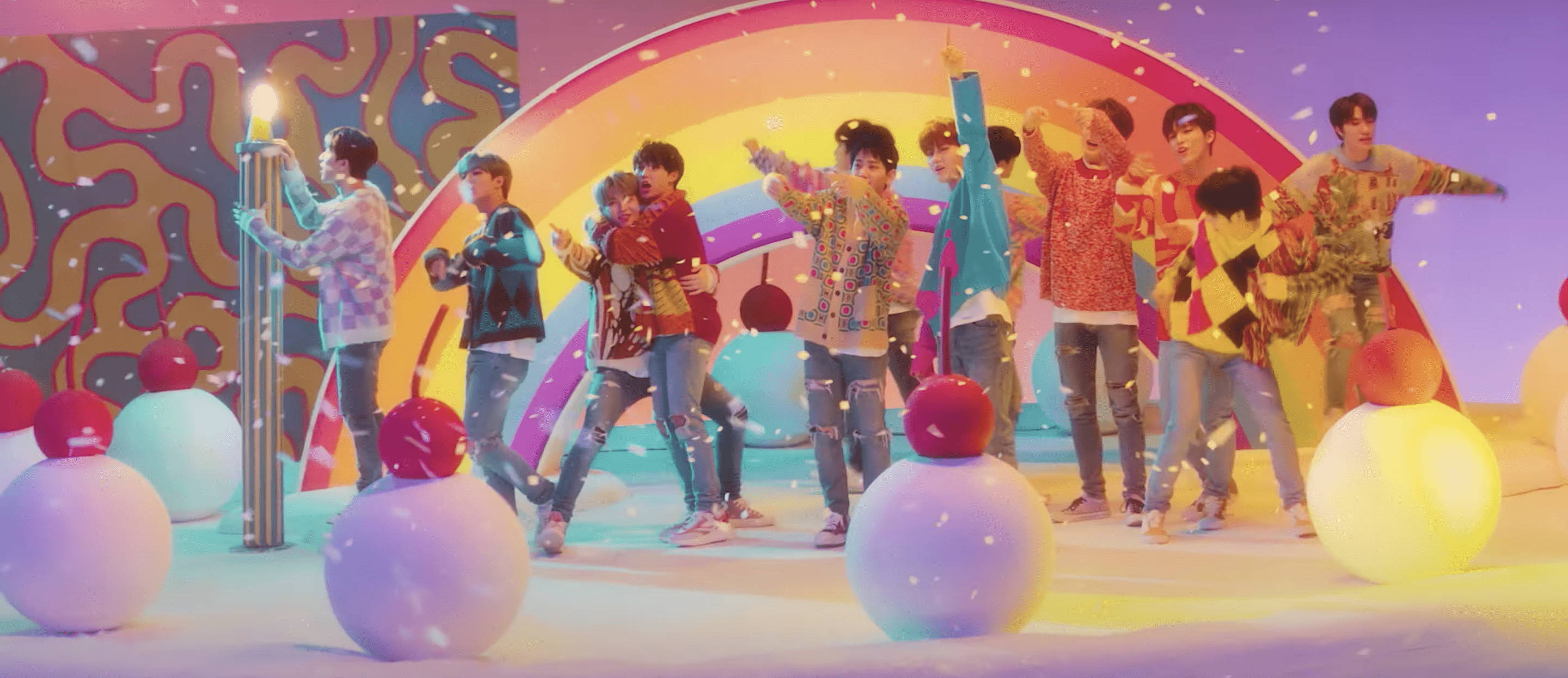 Treasure《My Treasure》MV 壁紙 — 一群充滿活力的年輕男子身穿色彩繽紛的服裝，在一個帶有巨型糖果狀球體和彩虹拱門的奇幻舞台上充滿活力地跳舞。