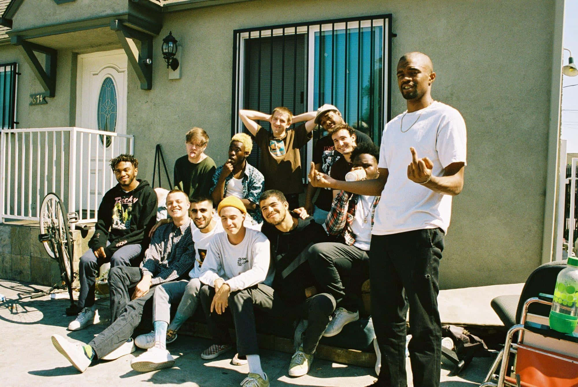 Brockhampton 桌布 壁紙 — 一群多元化的年輕男性在陽光普照的門廊上愉快地擺姿勢，身後有一間房子。