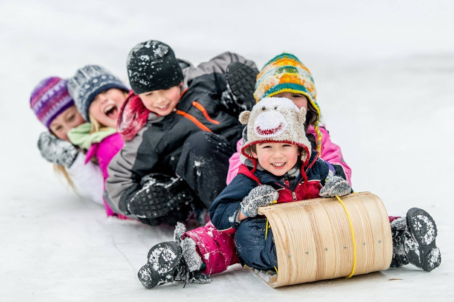 孩子們戴著冬季帽子和外套在雪丘上滑雪橇。