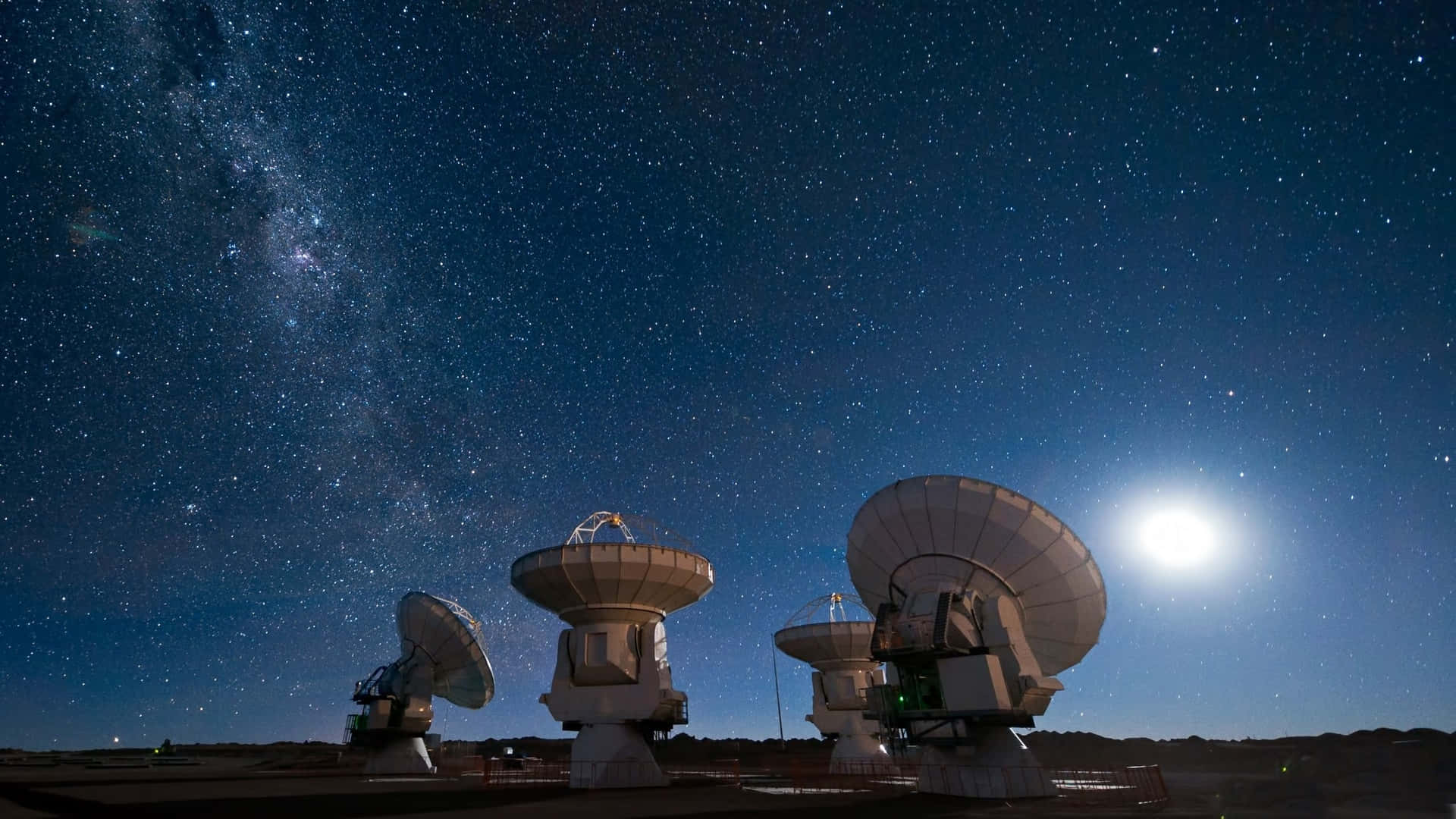 無線電望遠鏡在繁星點點的夜空中呈現剪影，銀河和月亮。