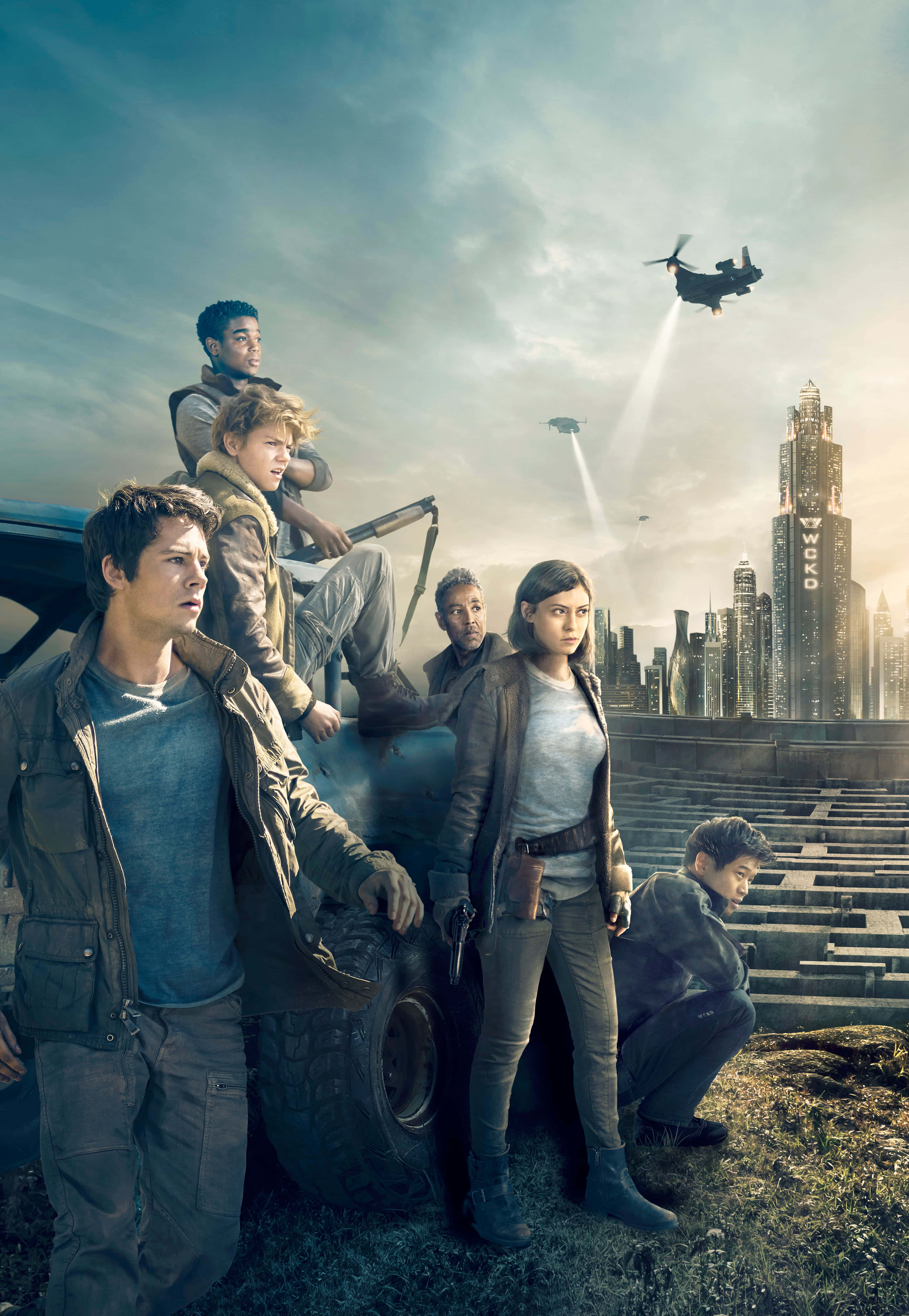 Maze Runner 桌布 壁紙 — 一群年輕的倖存者警覺地站在一輛堅固的車輛旁邊，背景是反烏托邦的城市景觀，頭頂有軍用飛行器飛過。