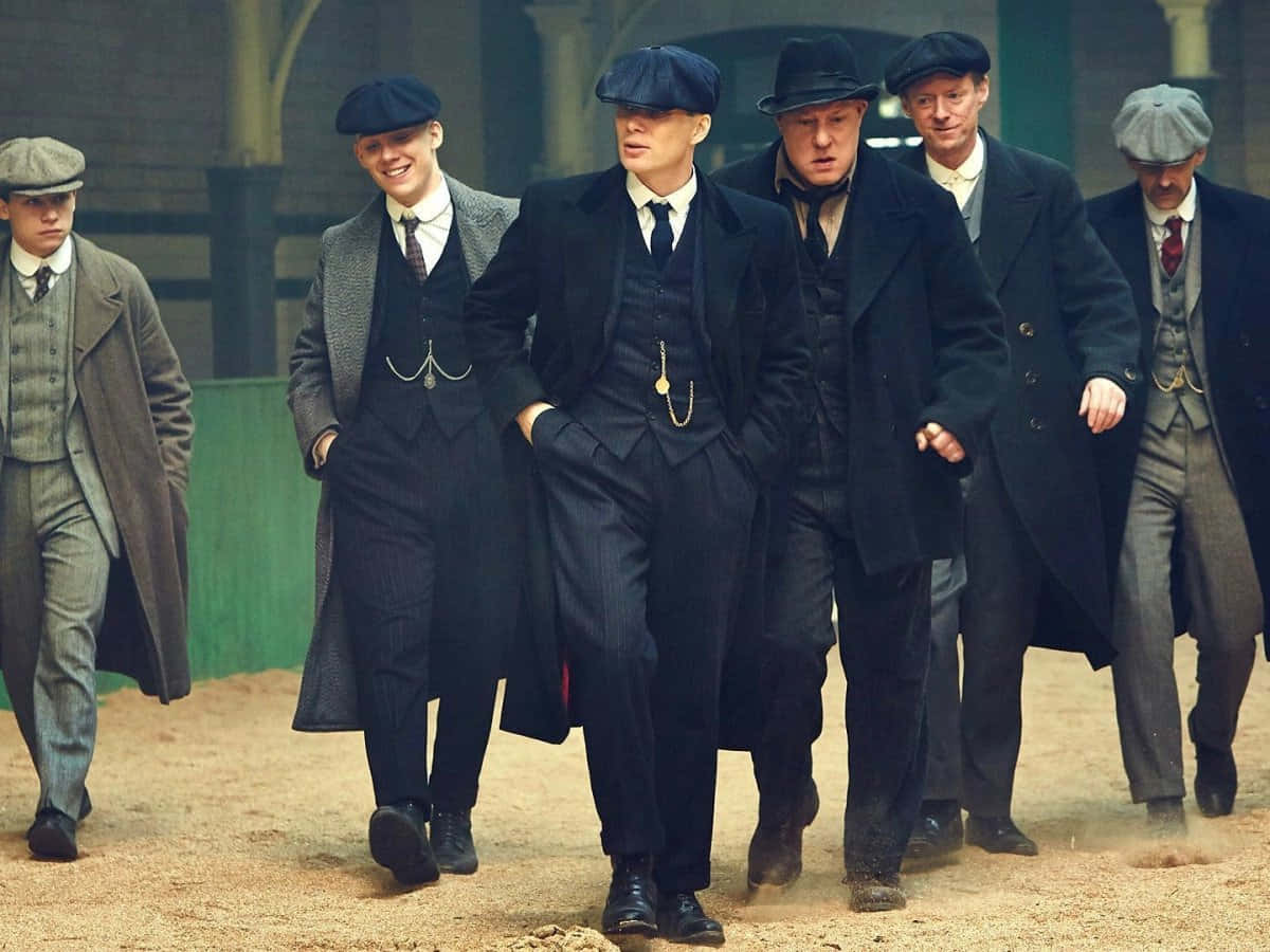 Peaky Blinders 桌布 壁紙 — 一群戴著復古平頂帽和穿著大衣的男人，在陰天下一條塵土飛揚的小徑上自信地大步走。