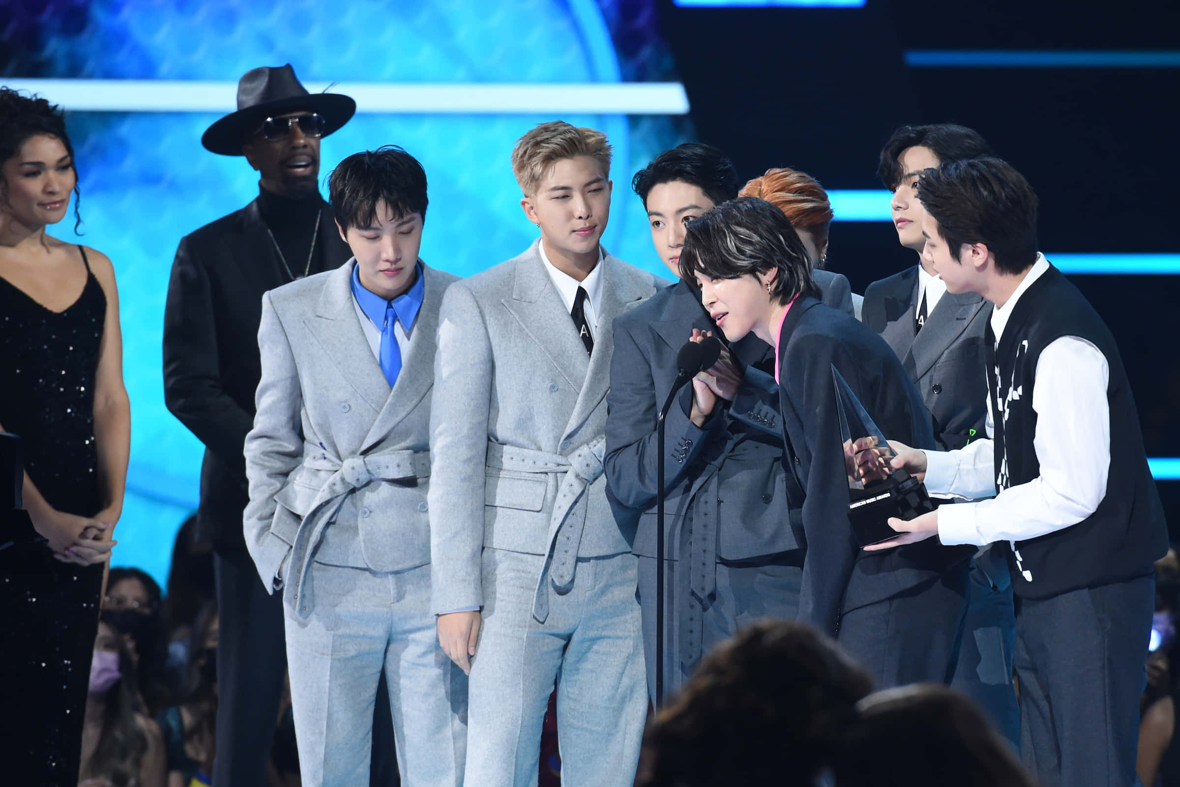 Namjoon 桌布 壁紙 — 一群時尚的K-pop偶像在燈光璀璨的舞台上，面帶微笑、身穿正式西裝領取獎項。