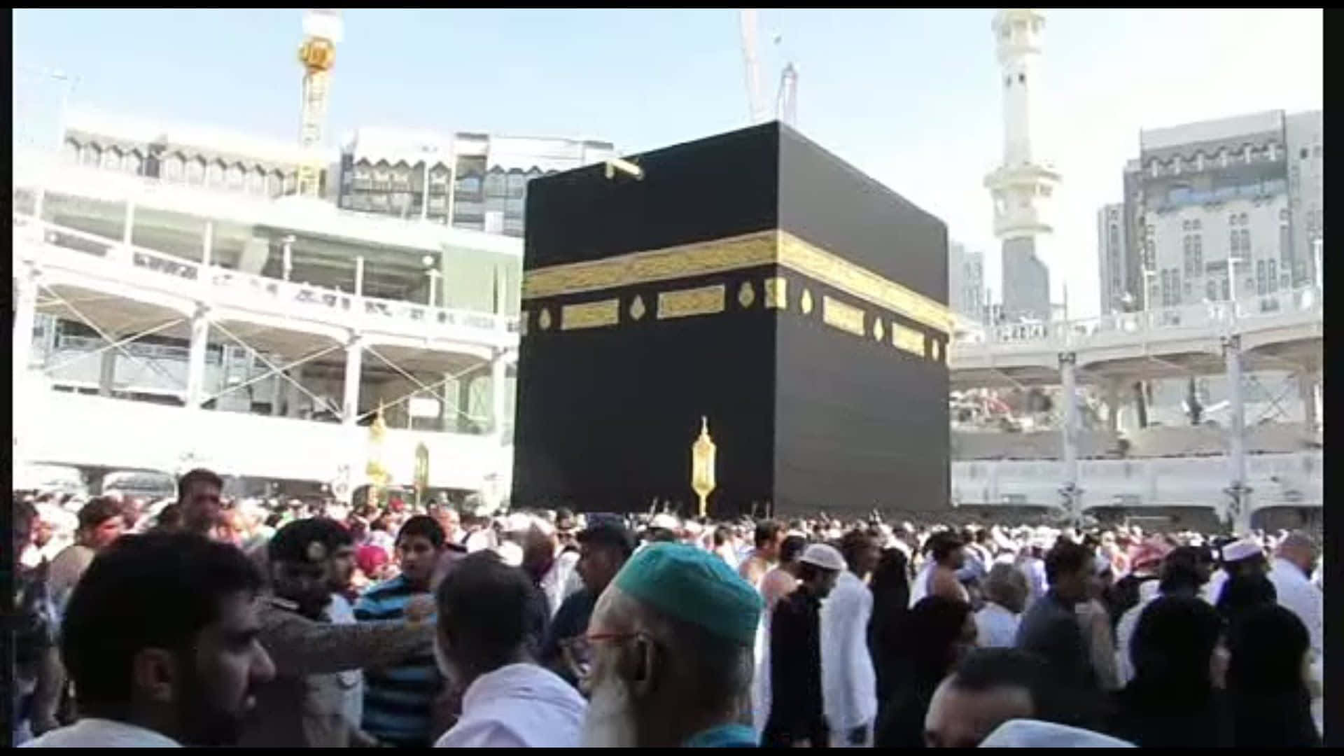 Makkah 桌布 壁紙 — 一群朝聖者在明亮的日光下圍繞著麥加的黑色的卡巴天房，背景有現代建築。