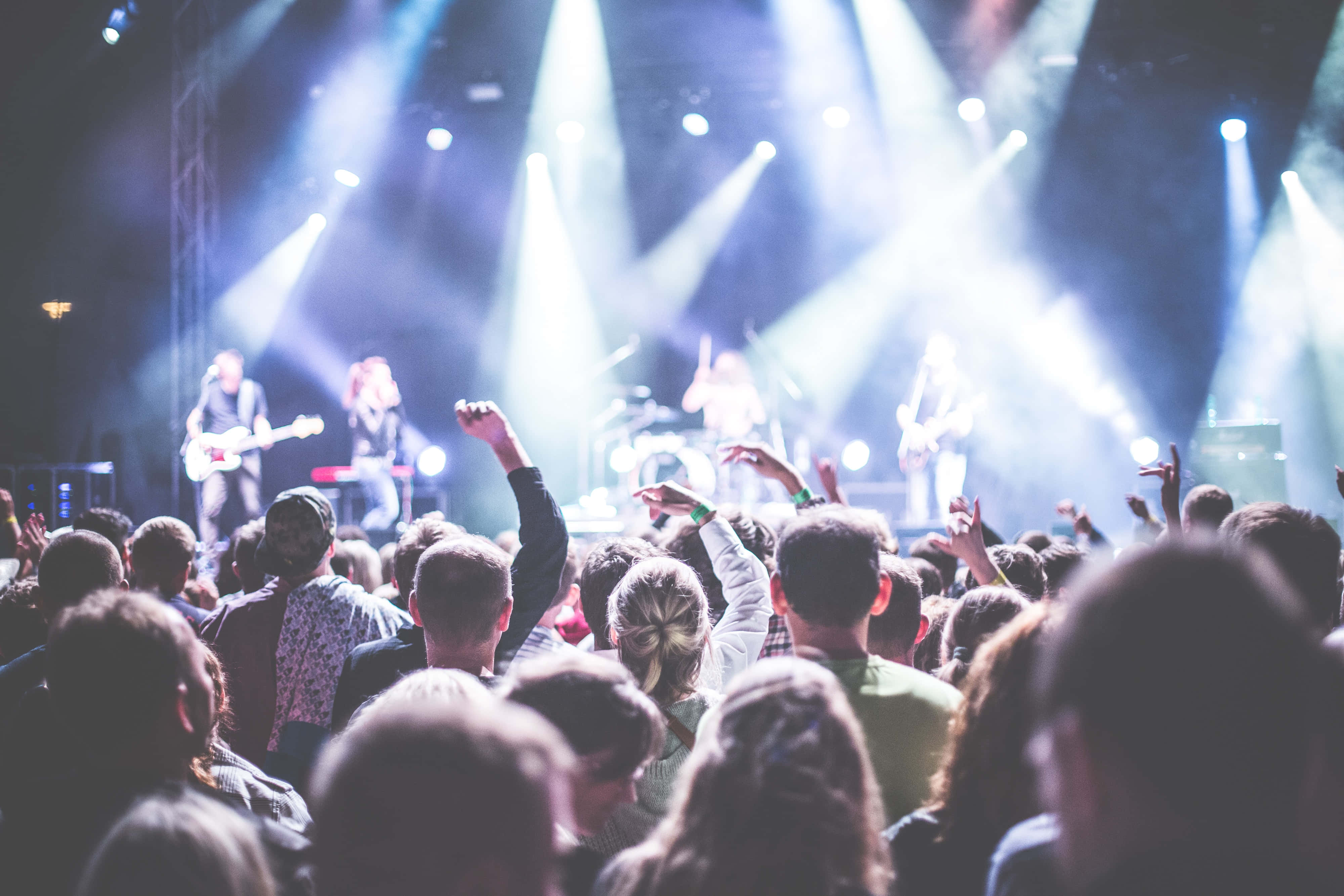 music festival 桌布 壁紙 — 一群演唱會觀眾舉起雙手，在明亮的白色舞台燈光下跳舞，現場音樂表演。