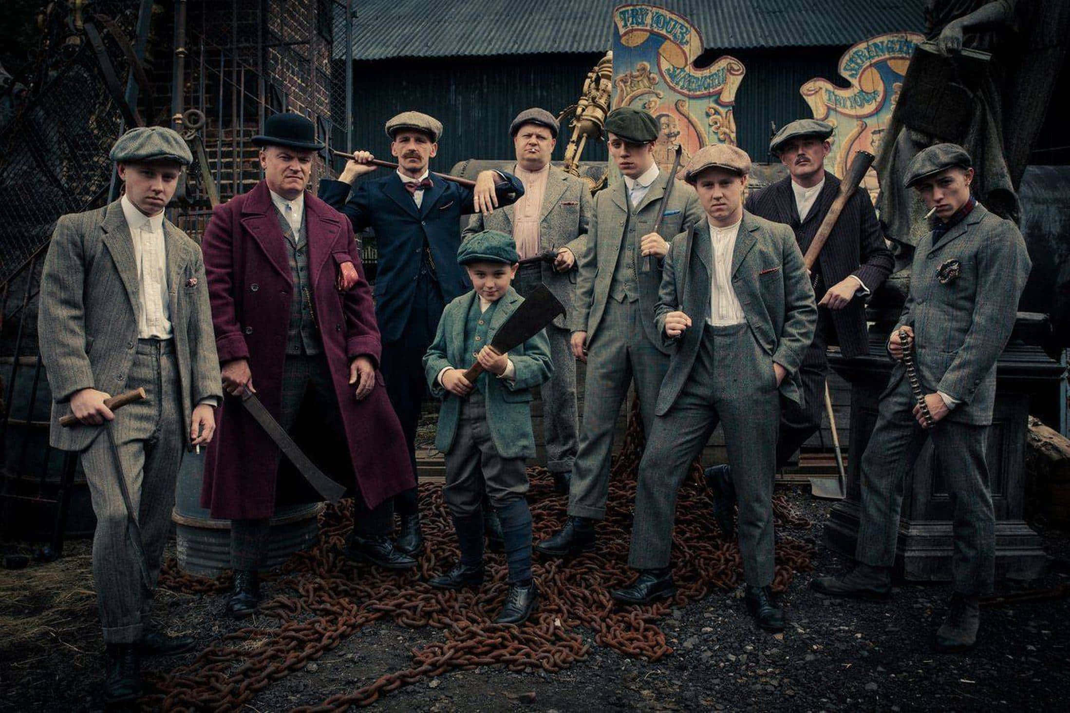 Peaky Blinders 桌布 壁紙 — 一群穿著1920年代西裝的男人和一個男孩，在工業場地手持武器和鎖鏈，氣勢洶洶地站著。