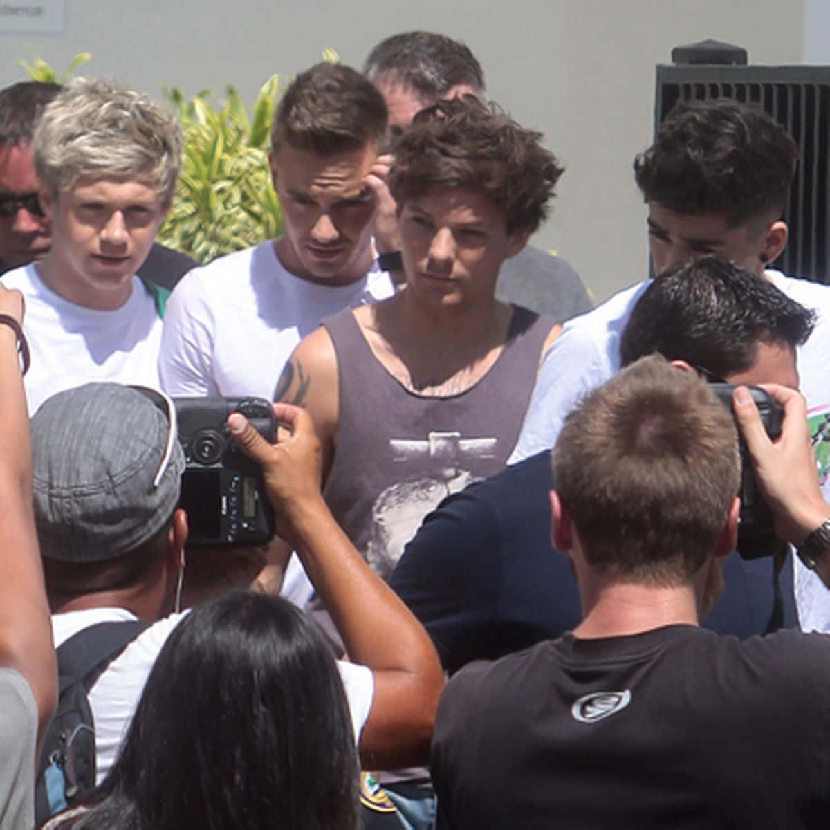One Direction 桌布 壁紙 — 一群穿著休閒服的年輕男子在明亮的日光下被攝影師包圍。