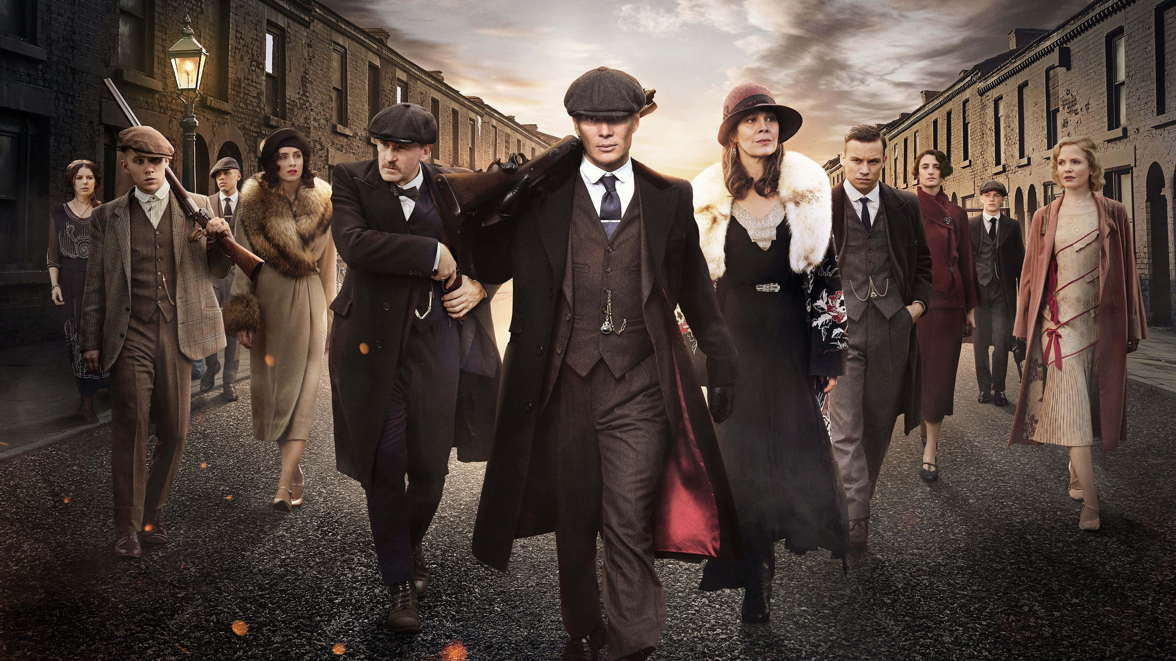 Peaky Blinders 桌布 壁紙 — 一群穿著時代服裝的角色在陰沉的暮色天空下，大步走過一條粗糙的城市街道。