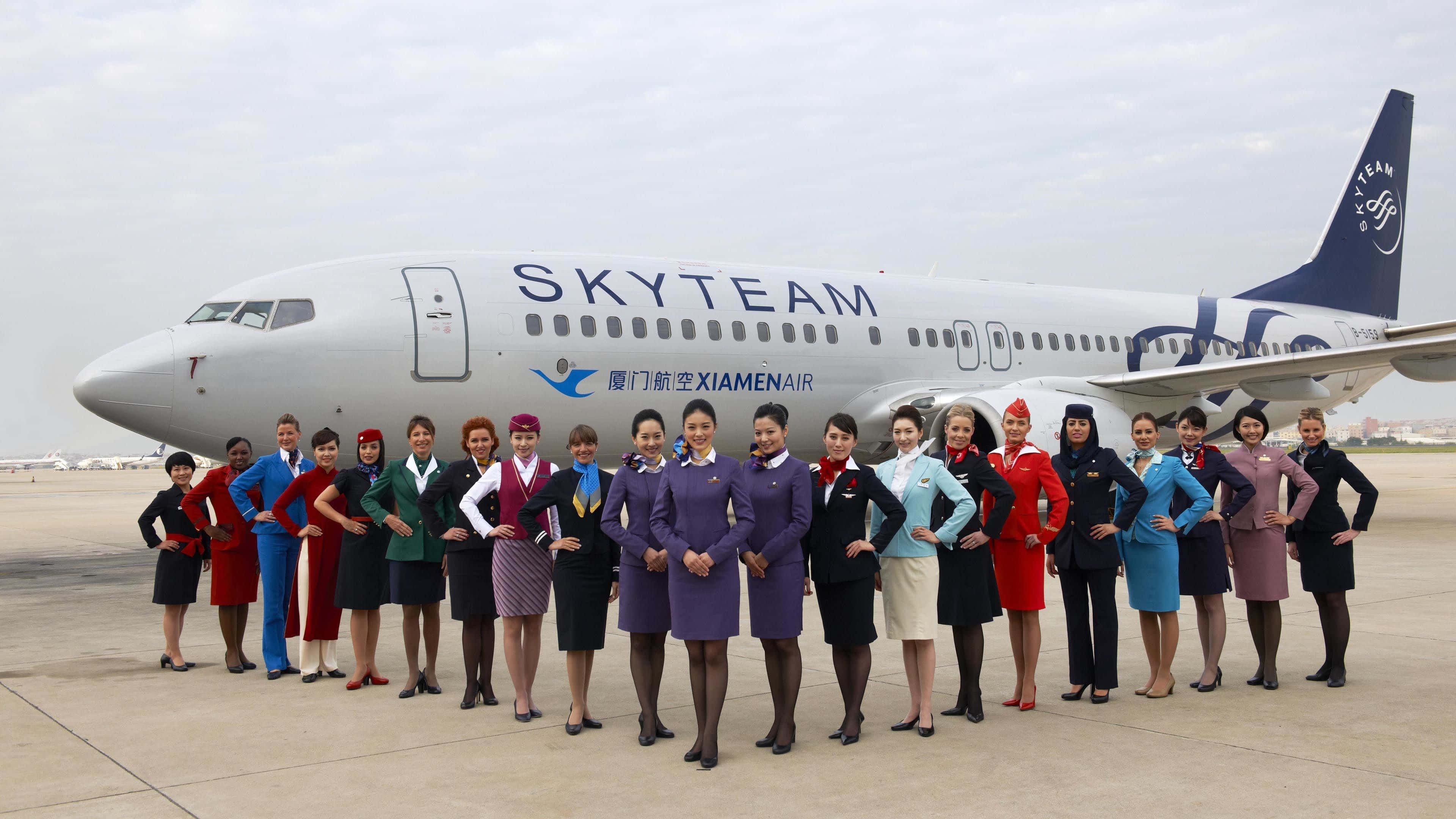 Flight Attendant 桌布 壁紙 — 一群穿著色彩繽紛制服的空服員在機場停機坪上，自信地在天合聯盟廈門航空飛機前擺姿勢。