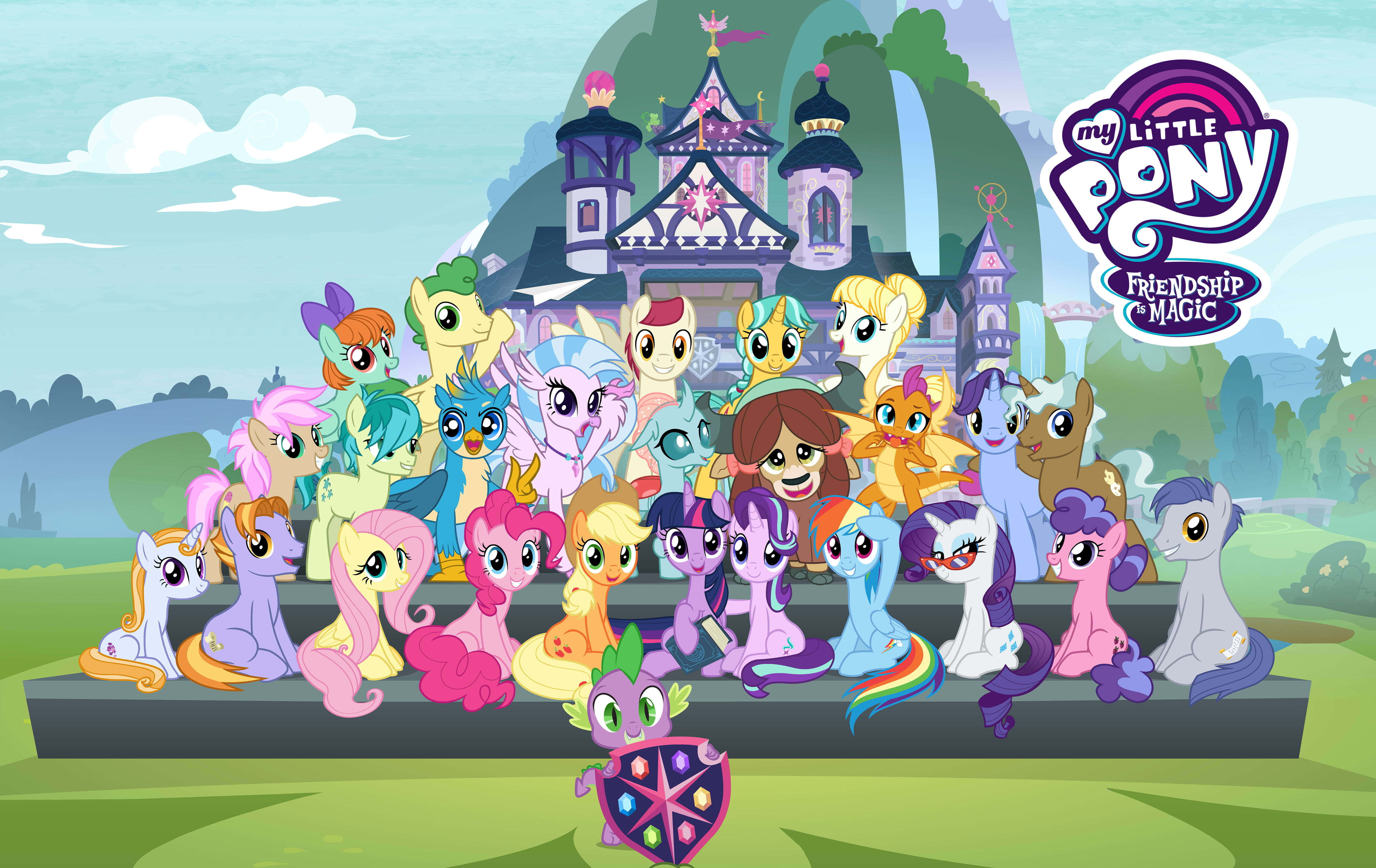 小馬寶莉 桌布 壁紙 — 一群色彩繽紛的卡通小馬和角色在明亮的粉彩風景中，在一個奇特的城堡前愉快地擺姿勢。