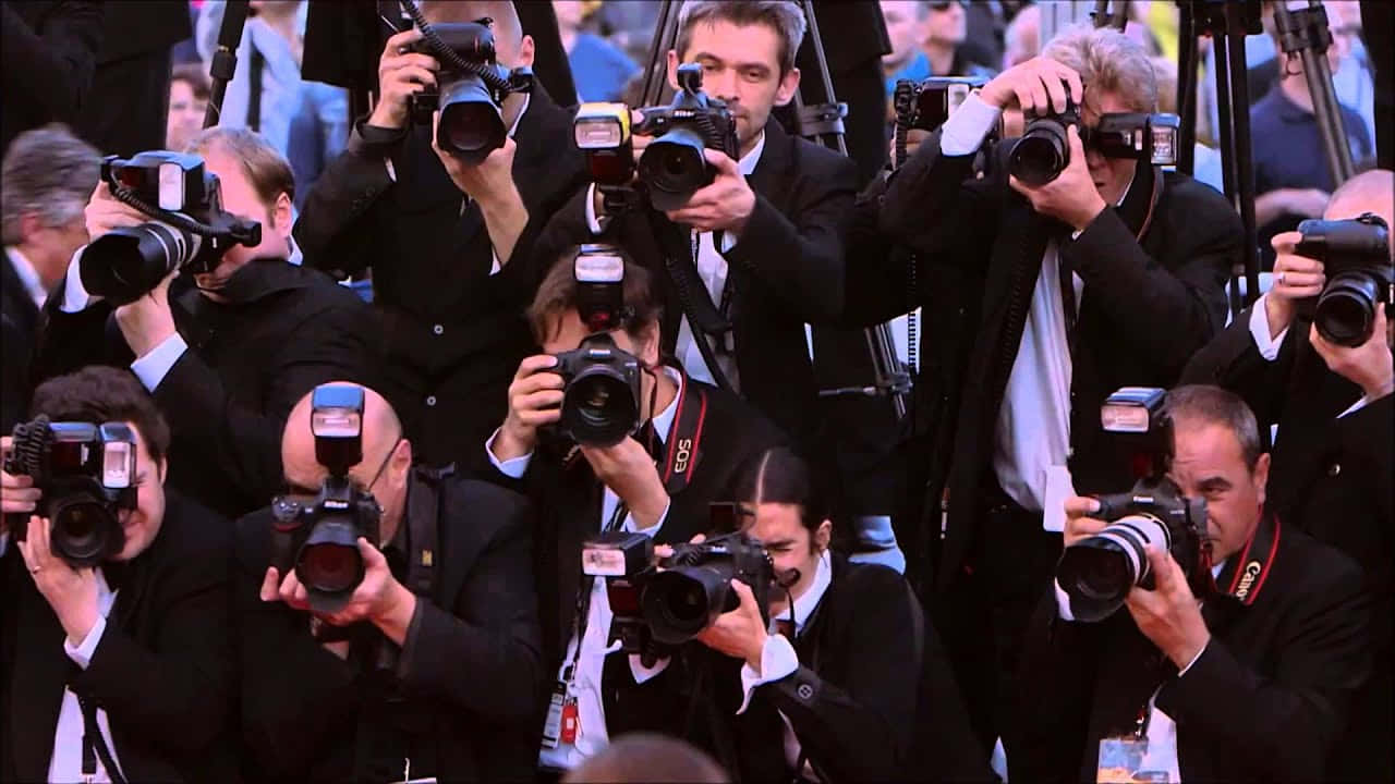 Paparazzi 桌布 壁紙 — 一群身穿黑色西裝的攝影師密集地將專業相機對準中央主體。
