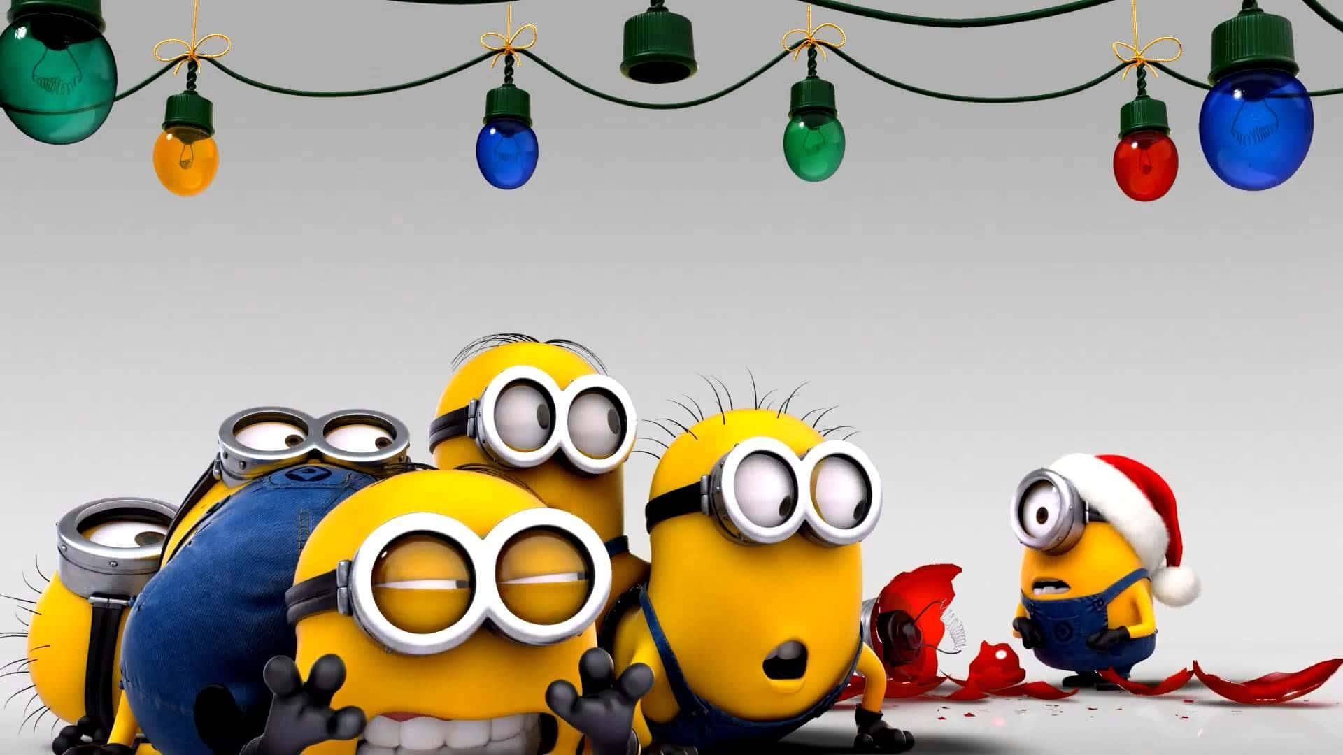 搞笑聖誕gif 桌布 壁紙 — 一群黃色嘅Minions戴住護目鏡，其中一個戴住聖誕老人帽，企喺色彩繽紛嘅聖誕燈下面。