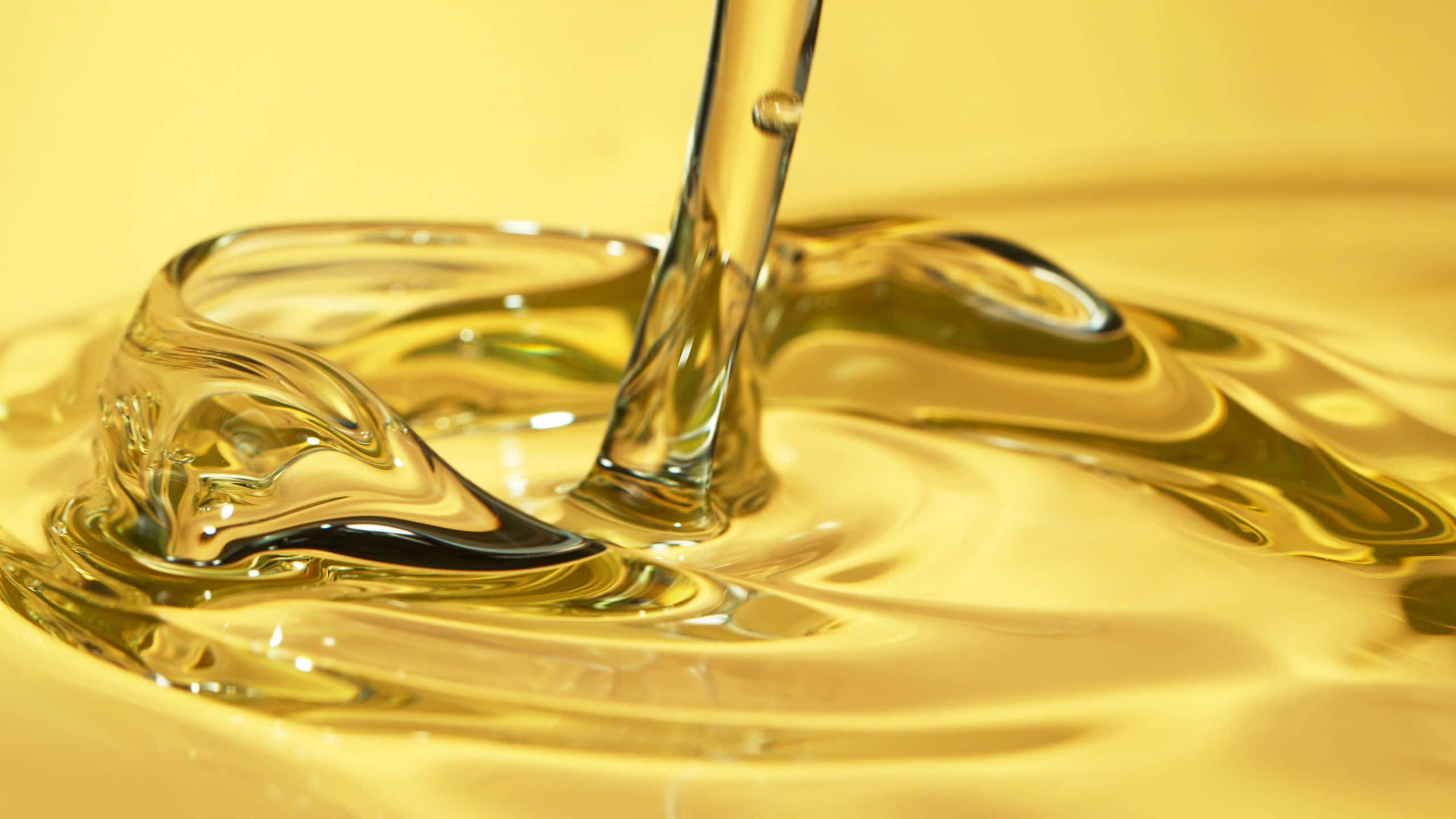 Oil 桌布 壁紙 — 一股金色油流傾瀉入池中，在溫暖的黃色背景下形成旋轉漣漪和光澤反射。