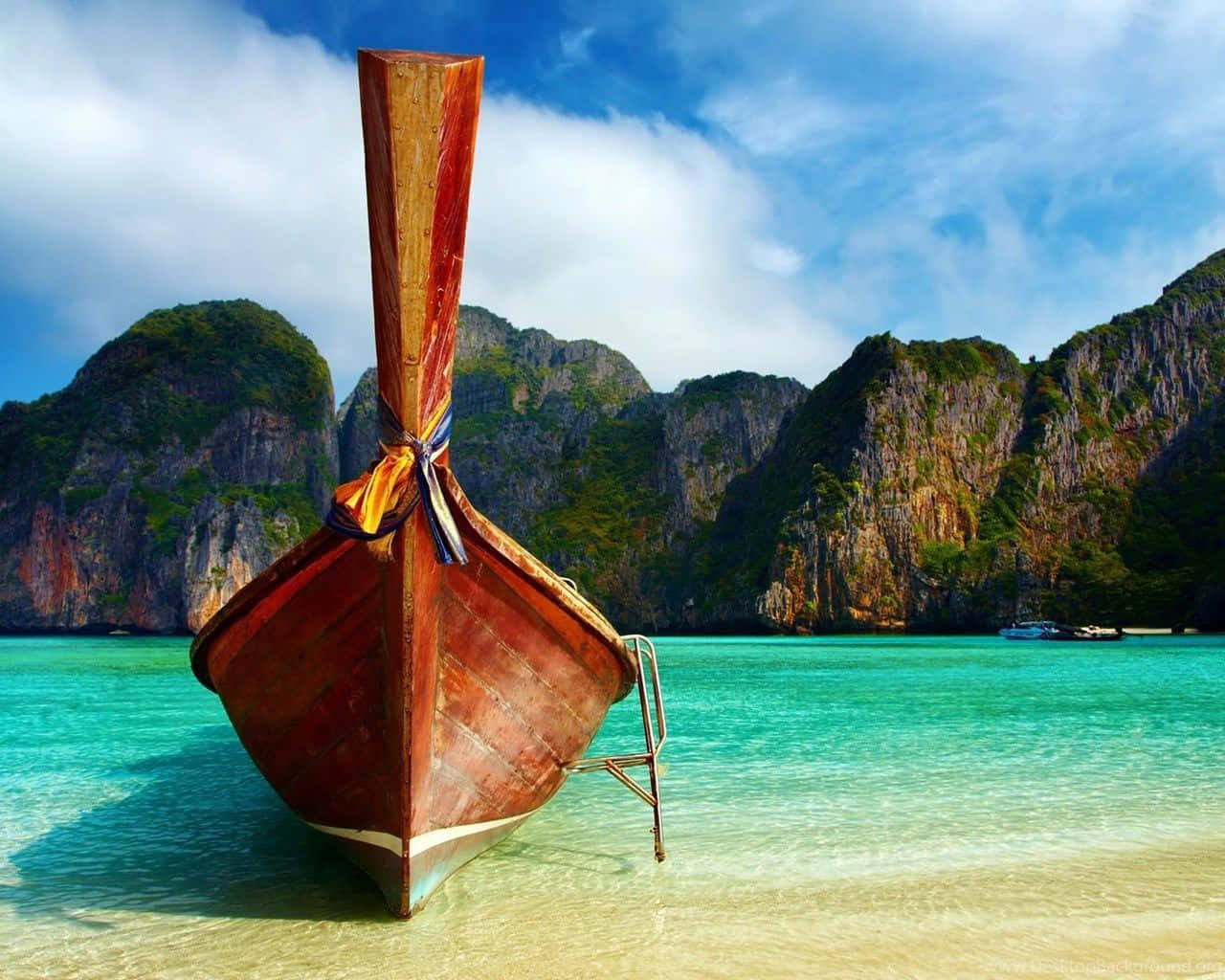 Thailand 桌布 壁紙 — 一艘傳統木製長尾船在清澈碧綠的海水中休憩，背景是鬱鬱蔥蔥的綠色懸崖，上方是明亮的藍天。