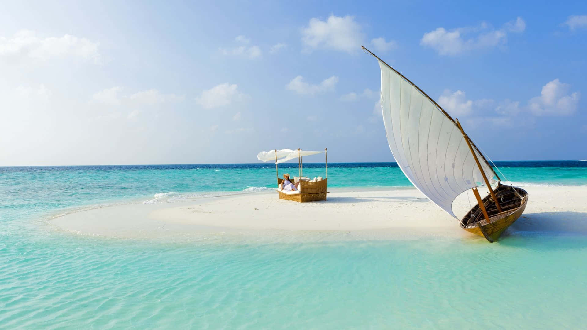Maldives Beach 桌布 壁紙 — 一艘傳統的單桅帆船停泊在純淨的白色沙洲上，四周是碧綠的海洋，頭頂是明亮的藍天。