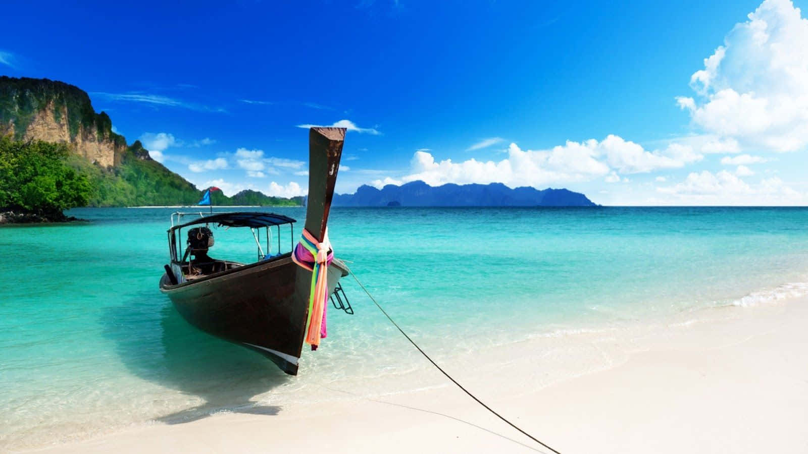 Thailand Beach 桌布 壁紙 — 一艘傳統長尾船停泊在 pristine 白色沙灘上，四周是碧綠的海水和鬱鬱蔥蔥的綠色懸崖，上方是明亮的藍天。