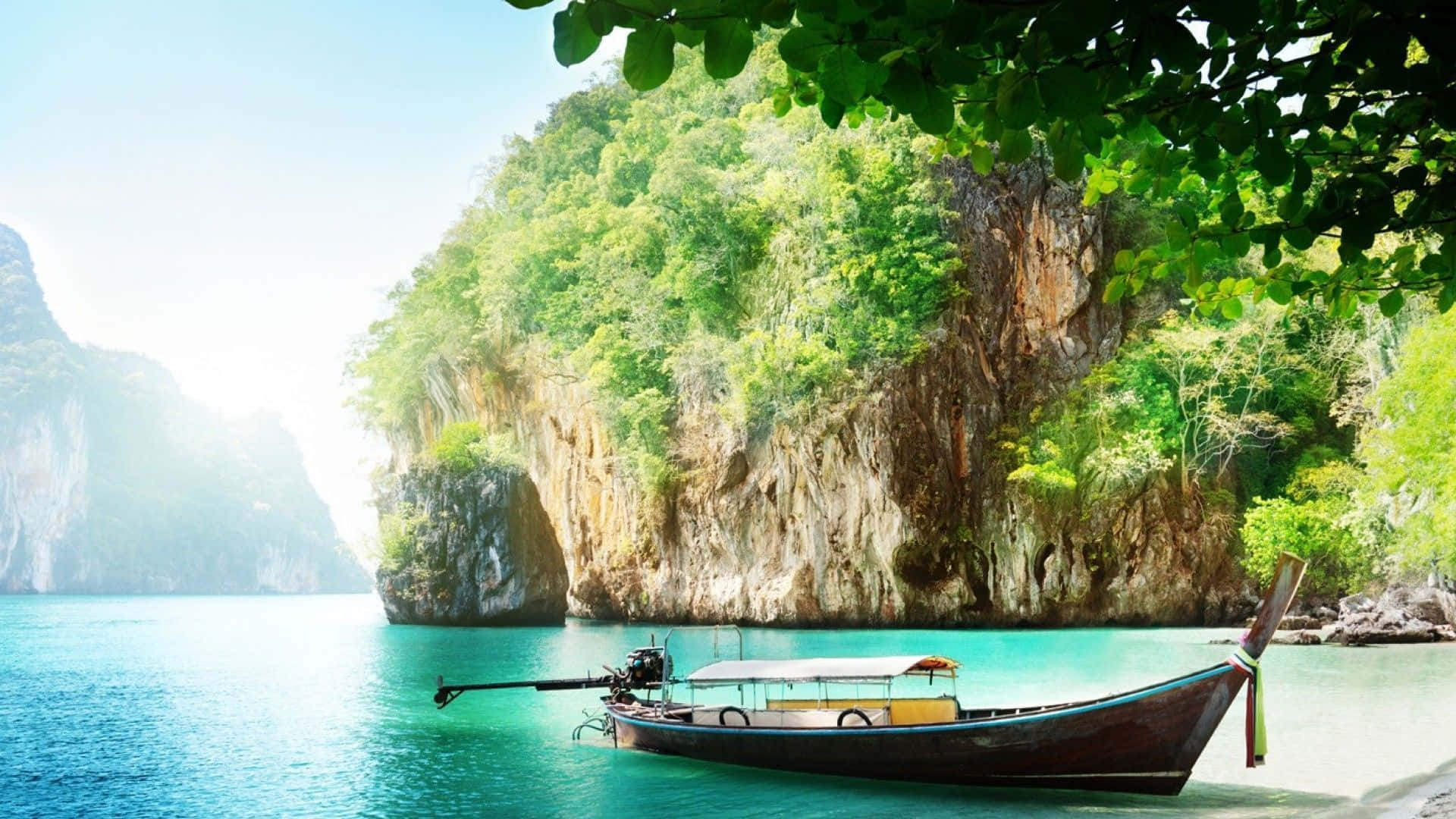 Thailand 桌布 壁紙 — 一艘傳統長尾船在明亮的日光下，停泊在碧綠海水旁，旁邊是鬱鬱蔥蔥的綠色懸崖。