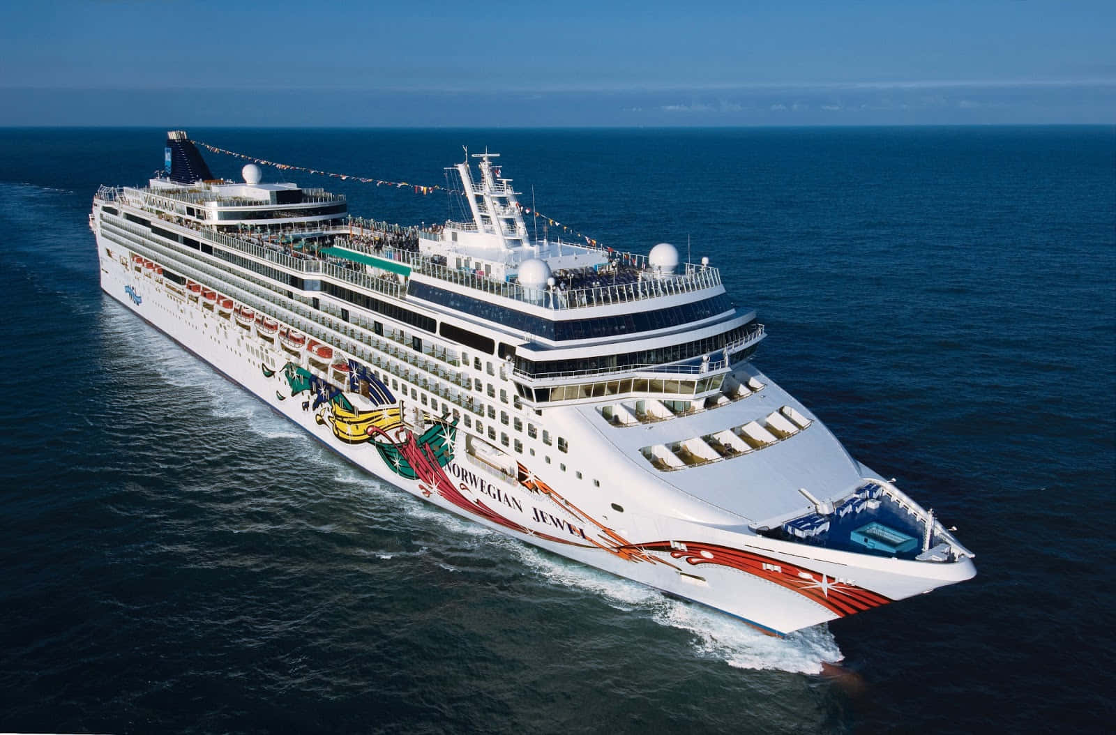 Ship 桌布 壁紙 — 一艘名為 Norwegian Jewel 的巨型白色郵輪在晴朗天空下航行於深藍色海洋，留下泡沫般的尾跡。
