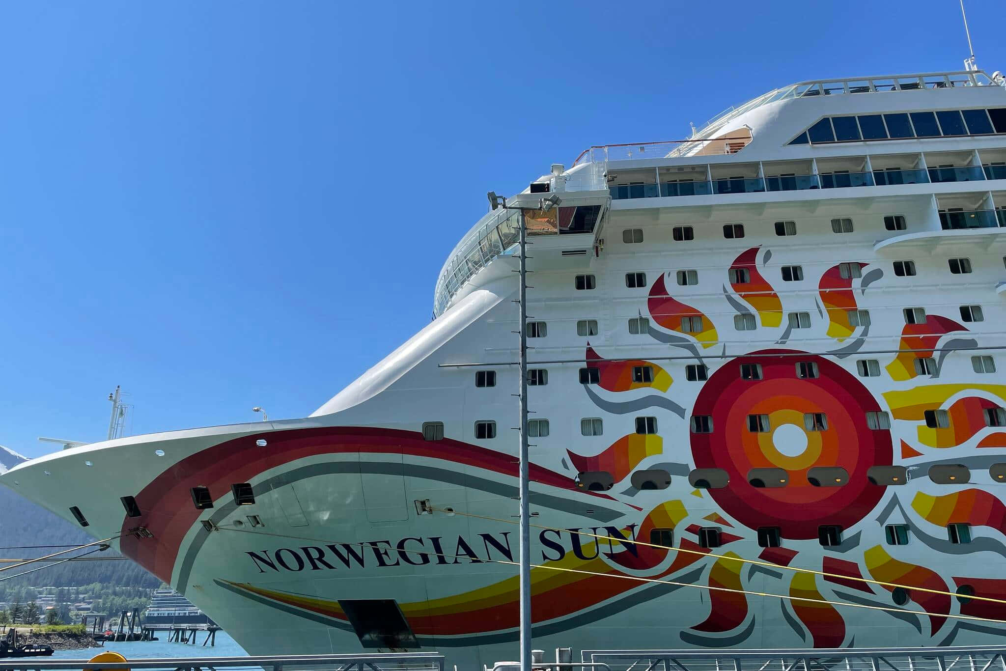 Cruise Ship 桌布 壁紙 — 一艘名為 Norwegian Sun 的巨型白色郵輪，帶有鮮豔的紅橙色太陽爆發壁畫，在清澈的藍天下佔據了畫面主導地位。
