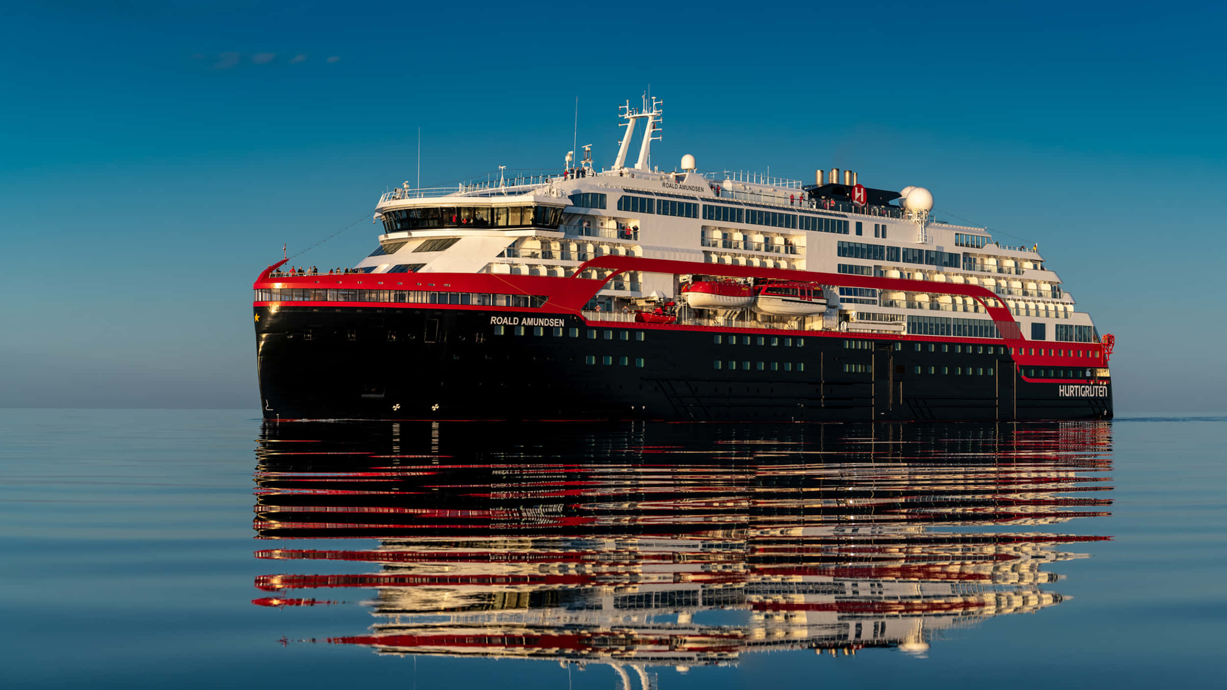 Cruise Ship 桌布 壁紙 — 一艘名為「Ronald Reagan」的紅黑相間大型郵輪，在晴朗的天空下，平靜的藍色水面上悠然漂浮，倒影完美。