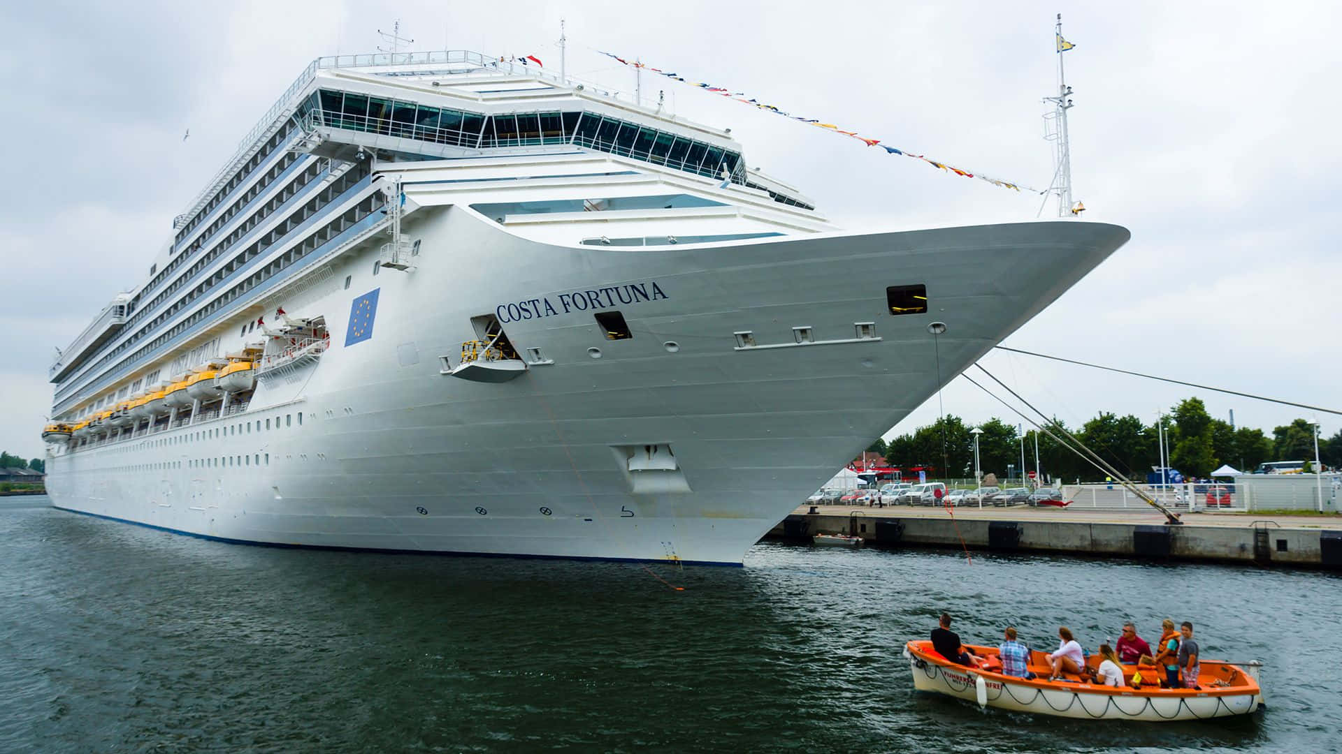 Cruise Ship 桌布 壁紙 — 一艘名為Costa Fortuna的巨型白色郵輪停靠在碼頭，附近有一艘載著乘客的橙色小船滑過。